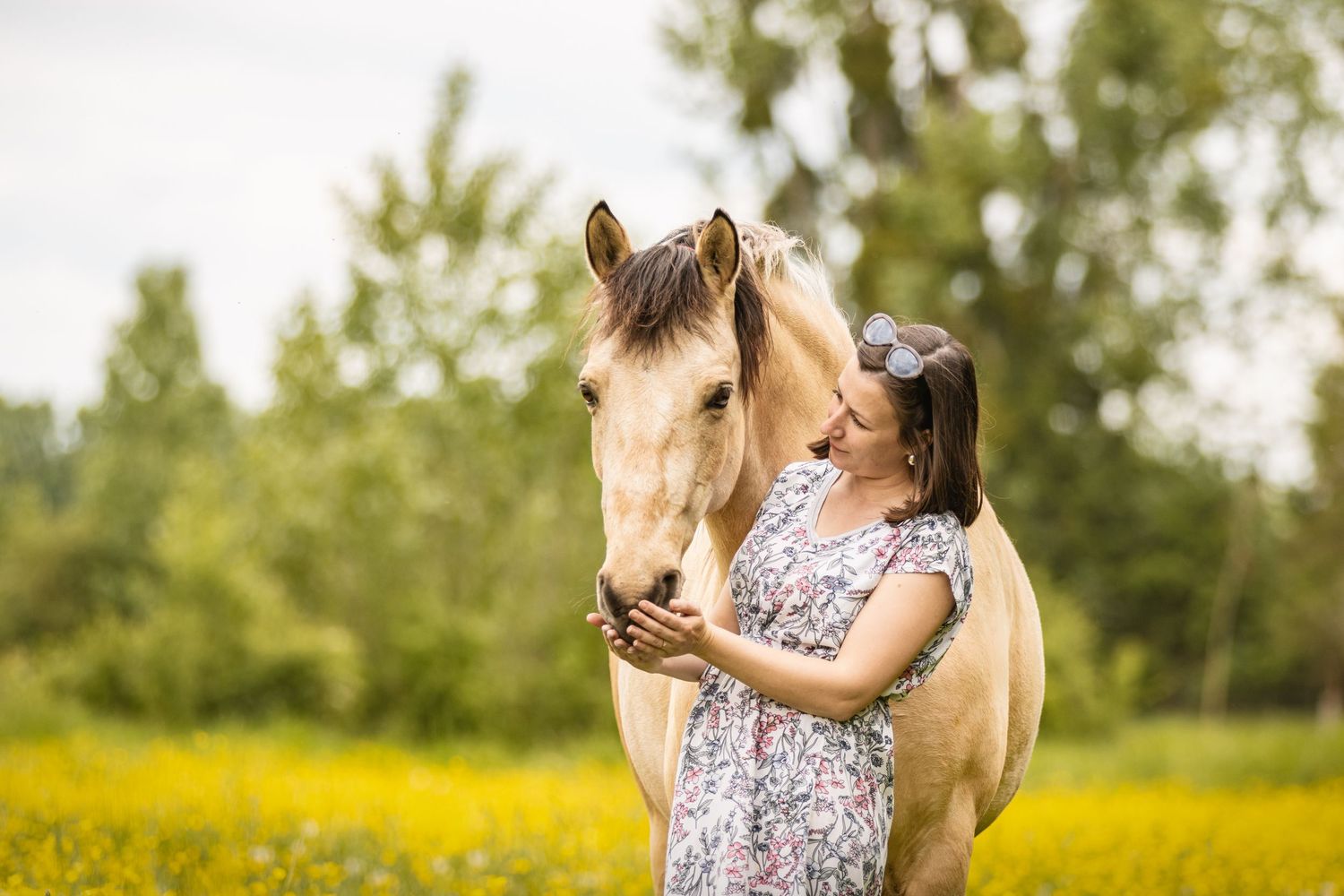 Young woman in floral dress tenderly embracing a palomino horse in a yellow wildflower field.