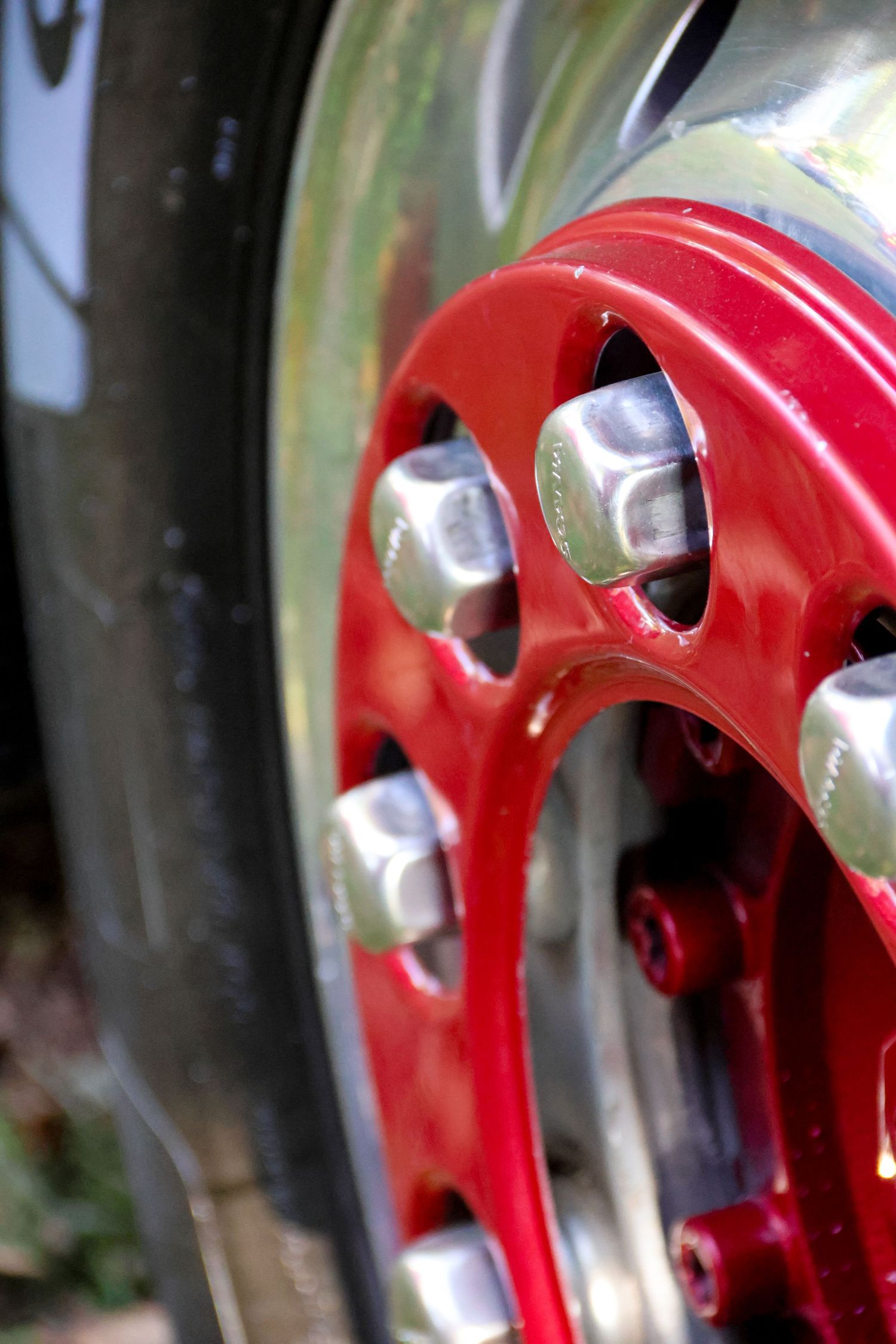 Close-up of a red and chrome wheel hub with silver lug nuts on a classic vintage vehicle tire.