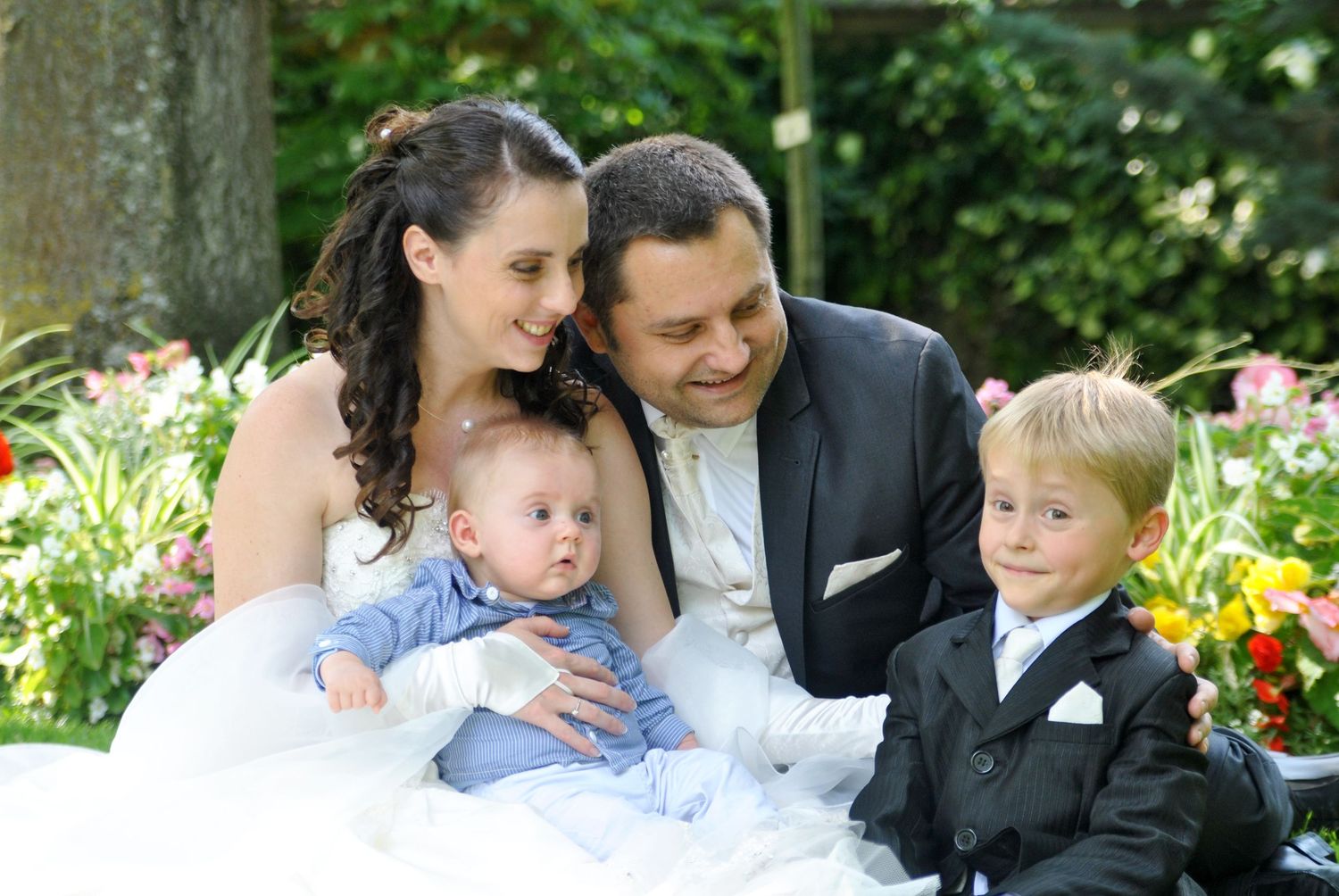 Happy wedding couple poses with baby and young boy in garden.