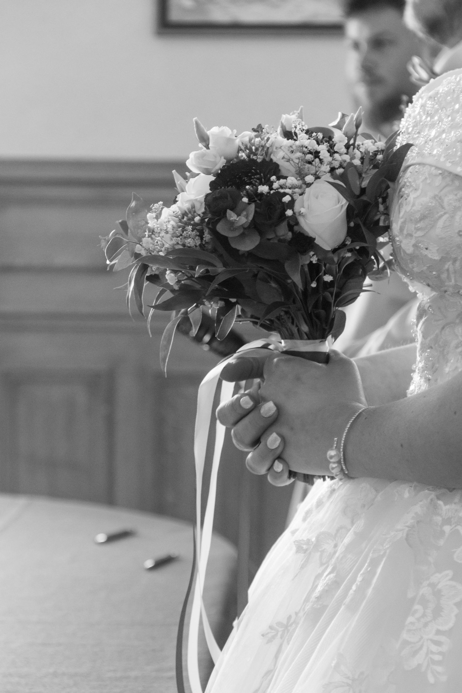 Black and white photo of a bride holding a floral bouquet with ribbons during a wedding ceremony.