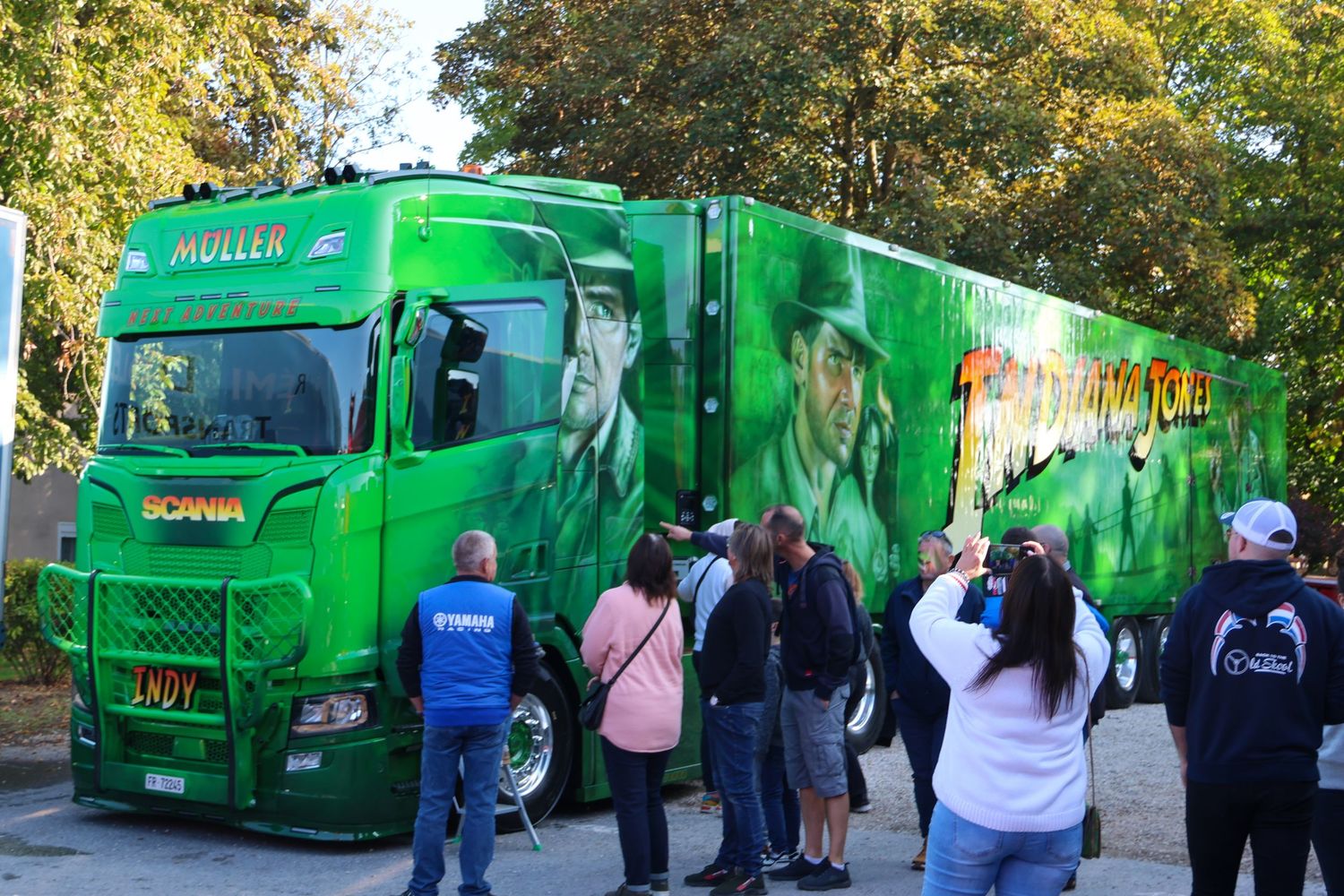 Crowd admires a green Scania Muller truck with dramatic character airbrush artwork at an outdoor show.