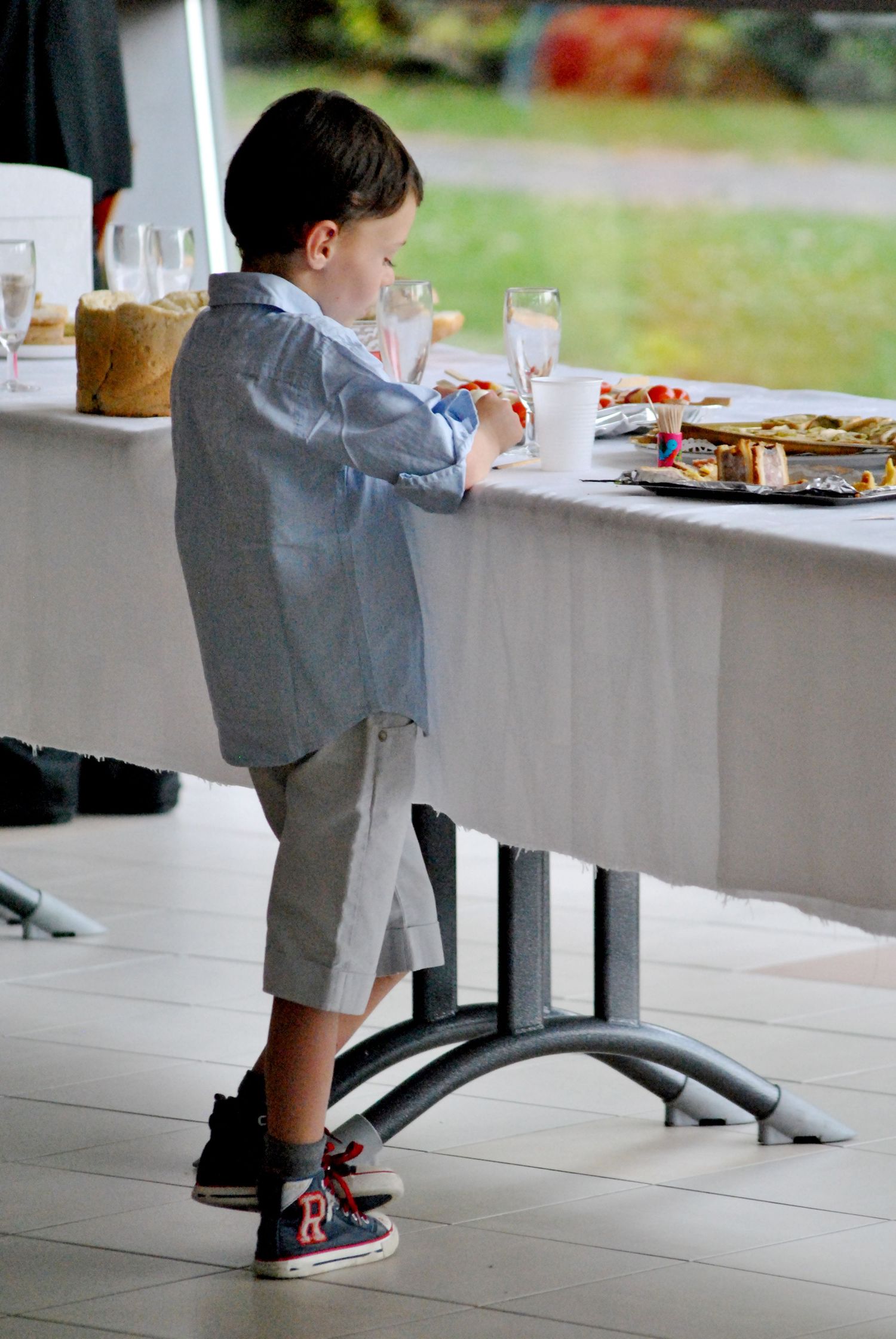 Young boy in formal attire reaching for food at elegant wedding reception table.