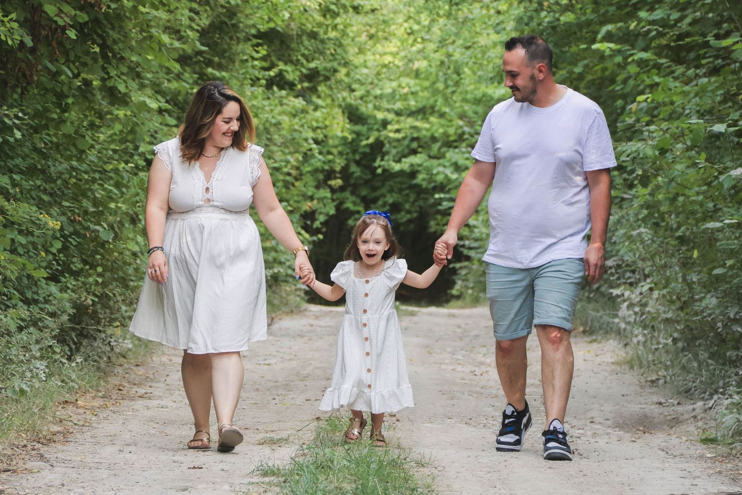 Séance famille lifestyle — famille avec une petite fille se promenant main dans la main sur un chemin arboré, photographe Guignicourt Aisne.