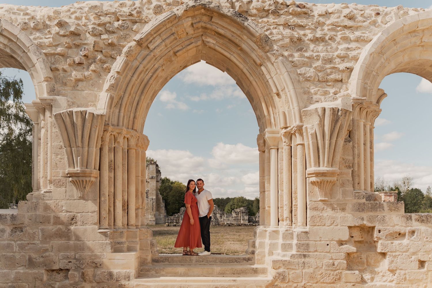 Couple embracing under ornate Gothic stone arches at ancient ruins on a sunny day.