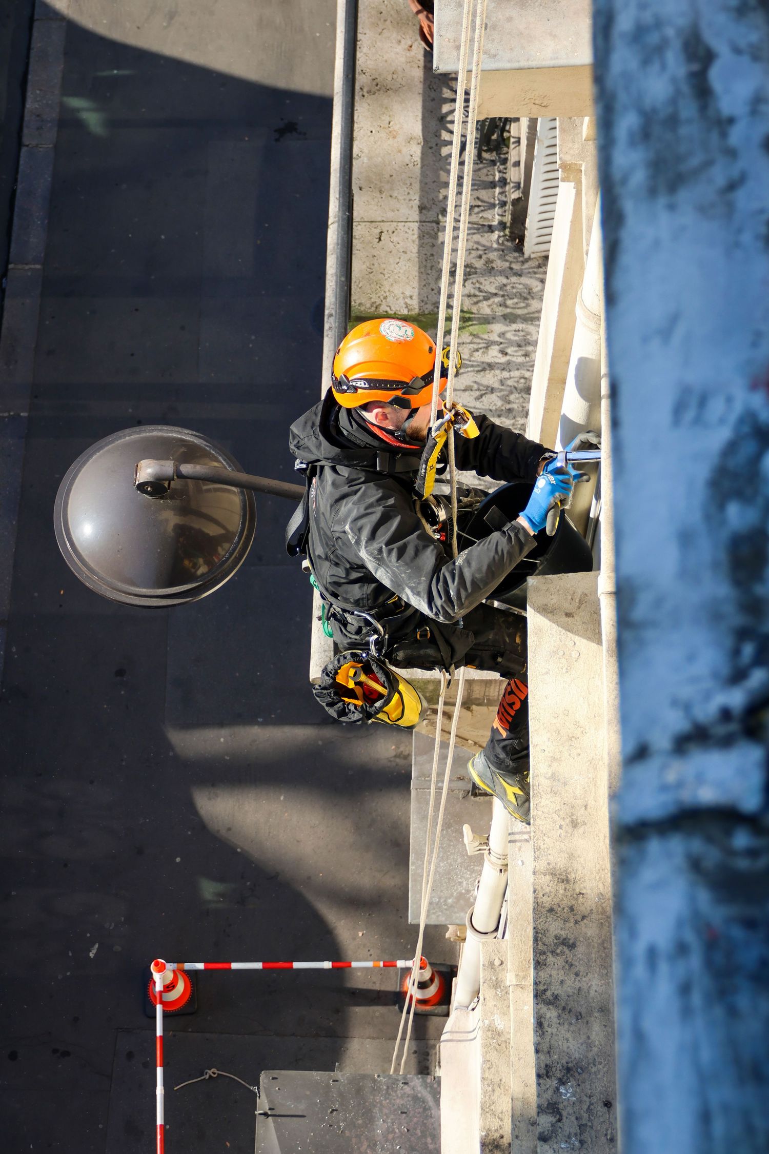 Industrial rope access worker in orange helmet rappelling down a building exterior for maintenance work.
