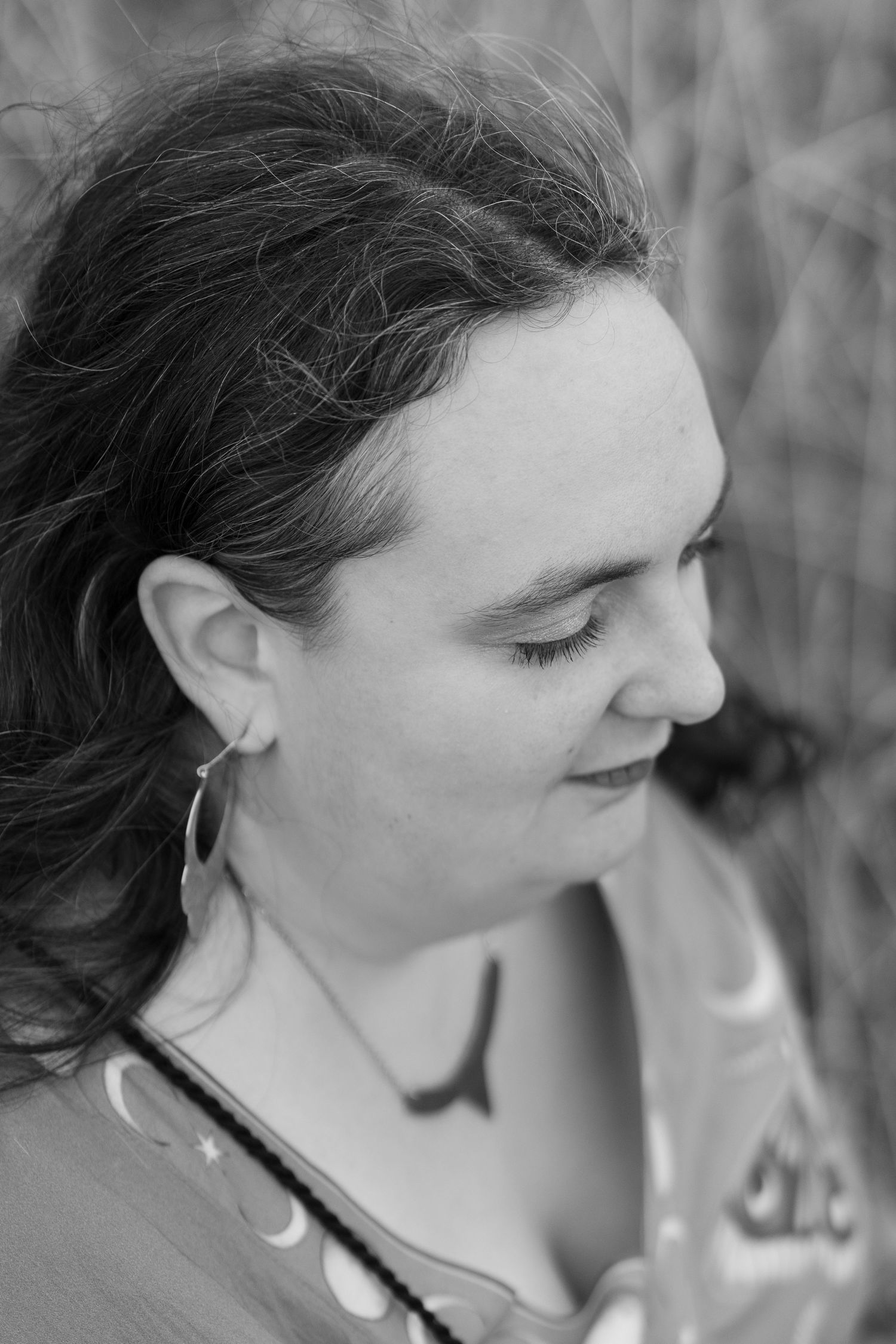Black and white portrait of woman with hoop earring looking down outdoors.