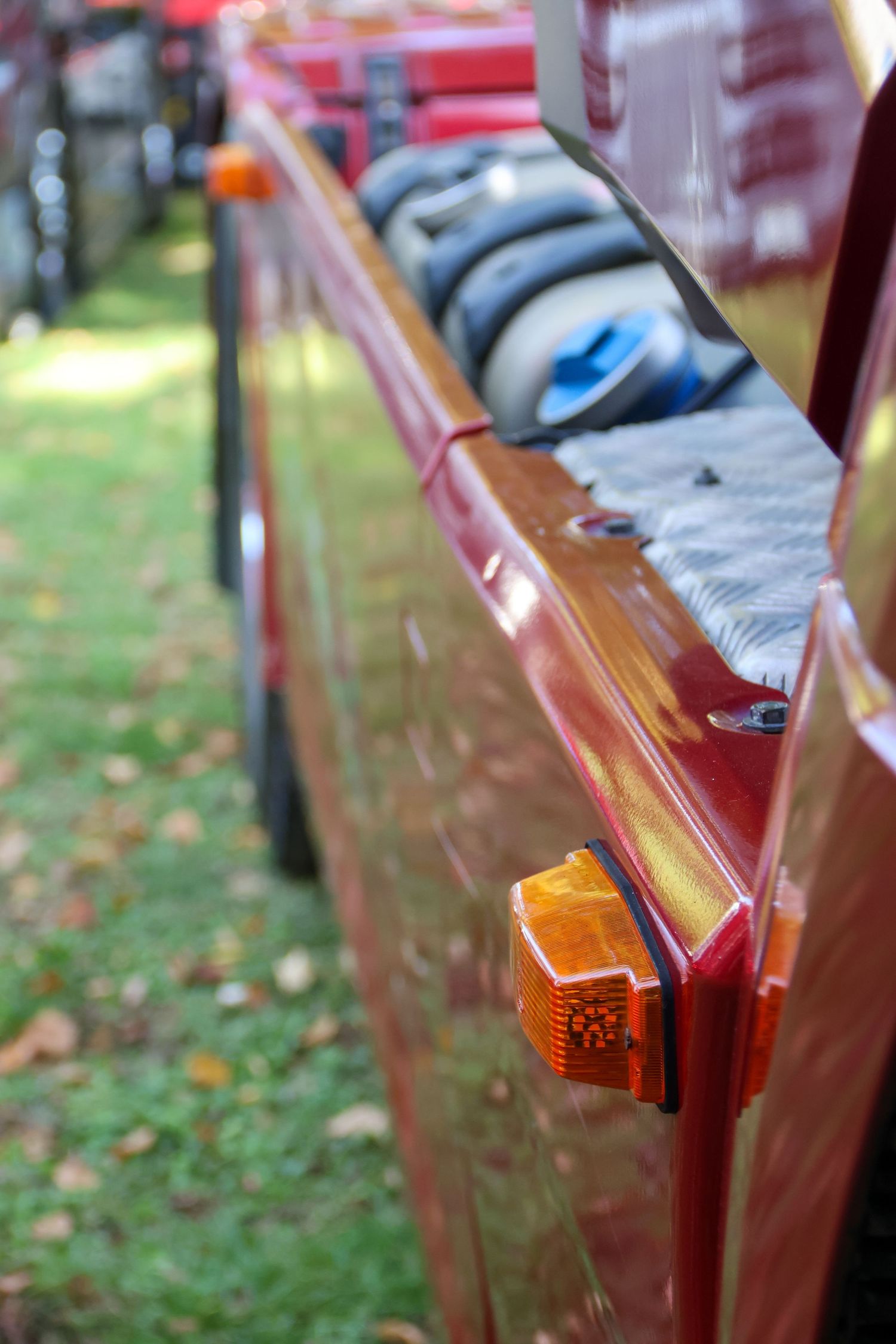 Close-up of a shiny red vehicle side panel featuring an amber turn signal light with luggage visible on the roof rack.