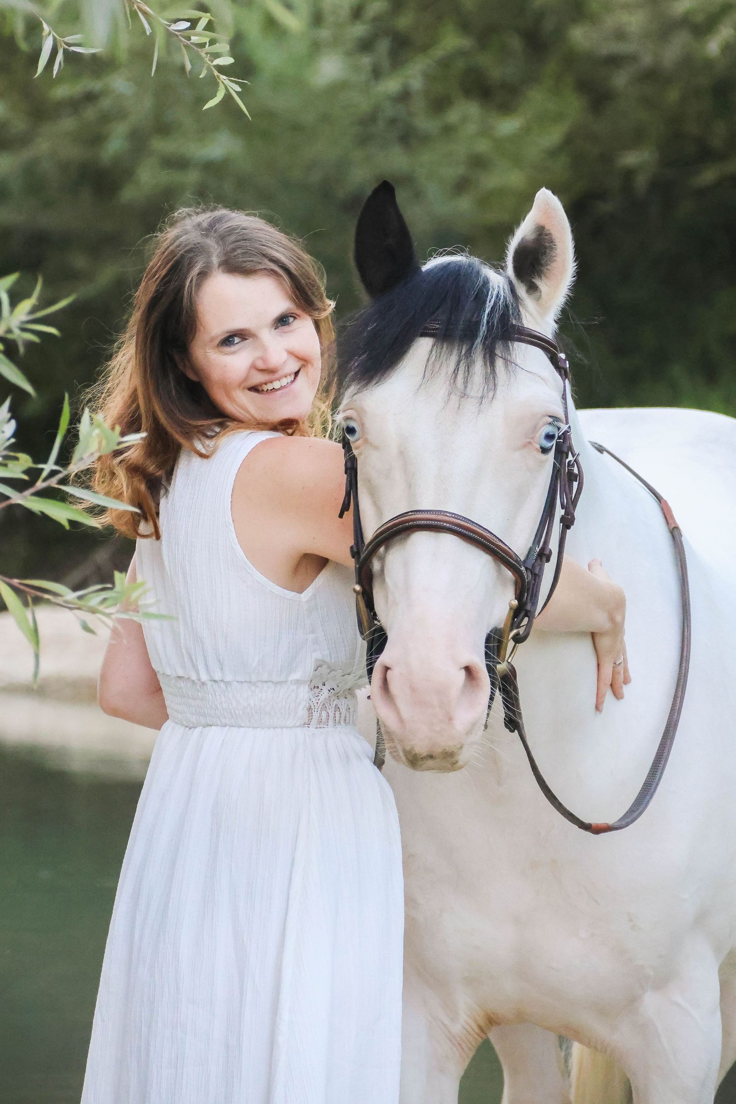 Séance animaux lifestyle — femme souriante en robe blanche aux côtés de son cheval pie en extérieur, photographe Soissons Laon Aisne.