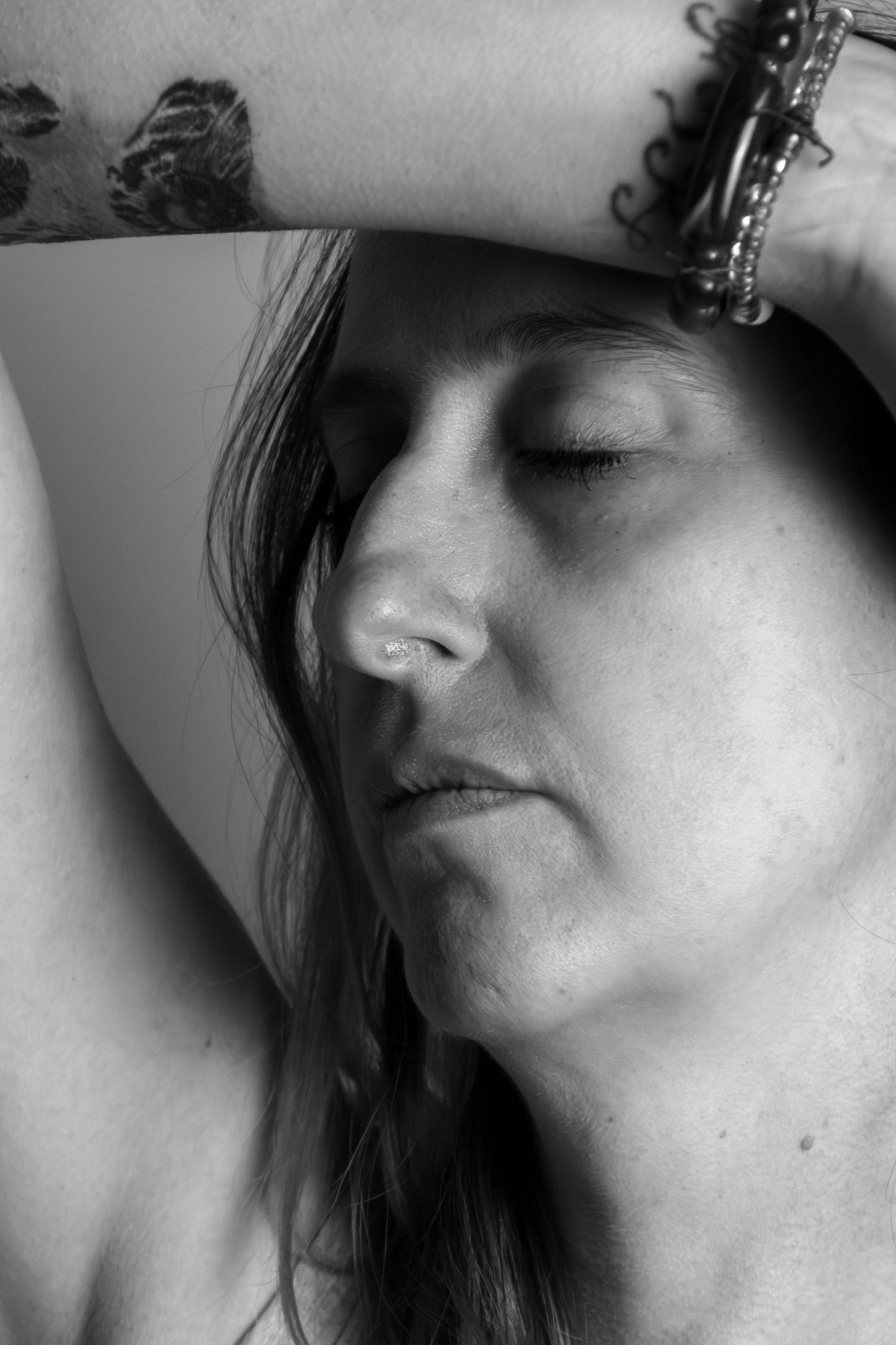 Séance Harmonie — portrait studio noir et blanc femme tatouée retenant ses cheveux en débardeur et bracelets, photographe Rethel Ardennes.