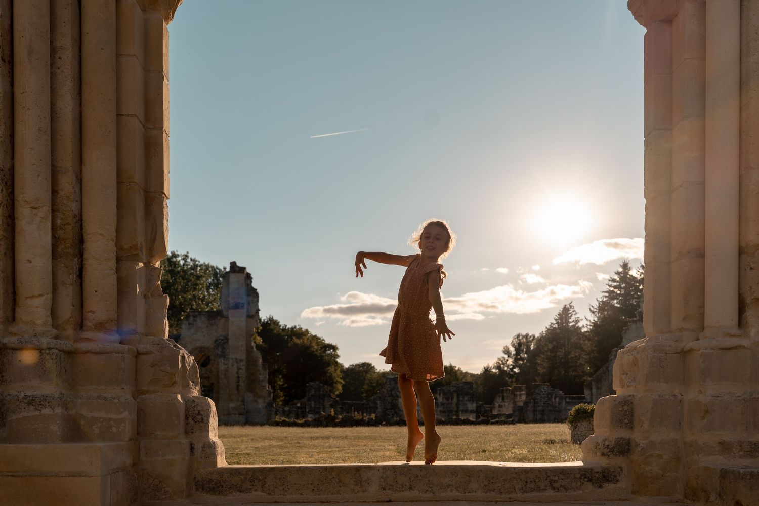 Silhouette of a woman dancing gracefully between stone columns at sunset in a historic outdoor plaza.