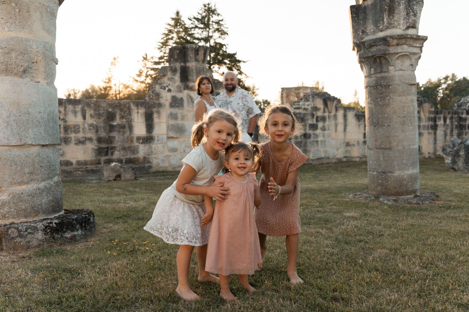 A happy family with three young children poses barefoot among ancient stone ruins at sunset.
