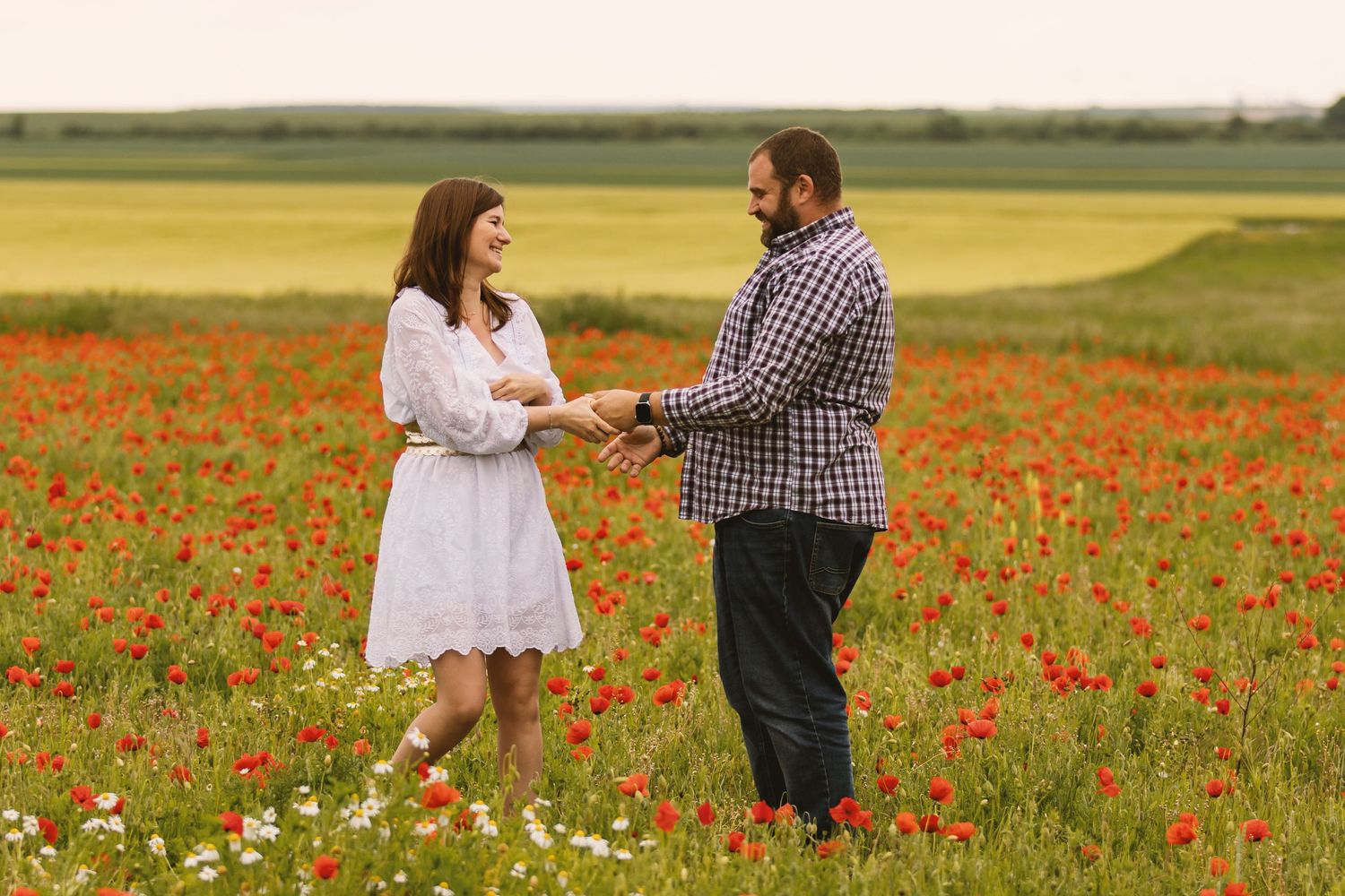 Romantic couple holding hands in a blooming red poppy field on a cloudy day.
