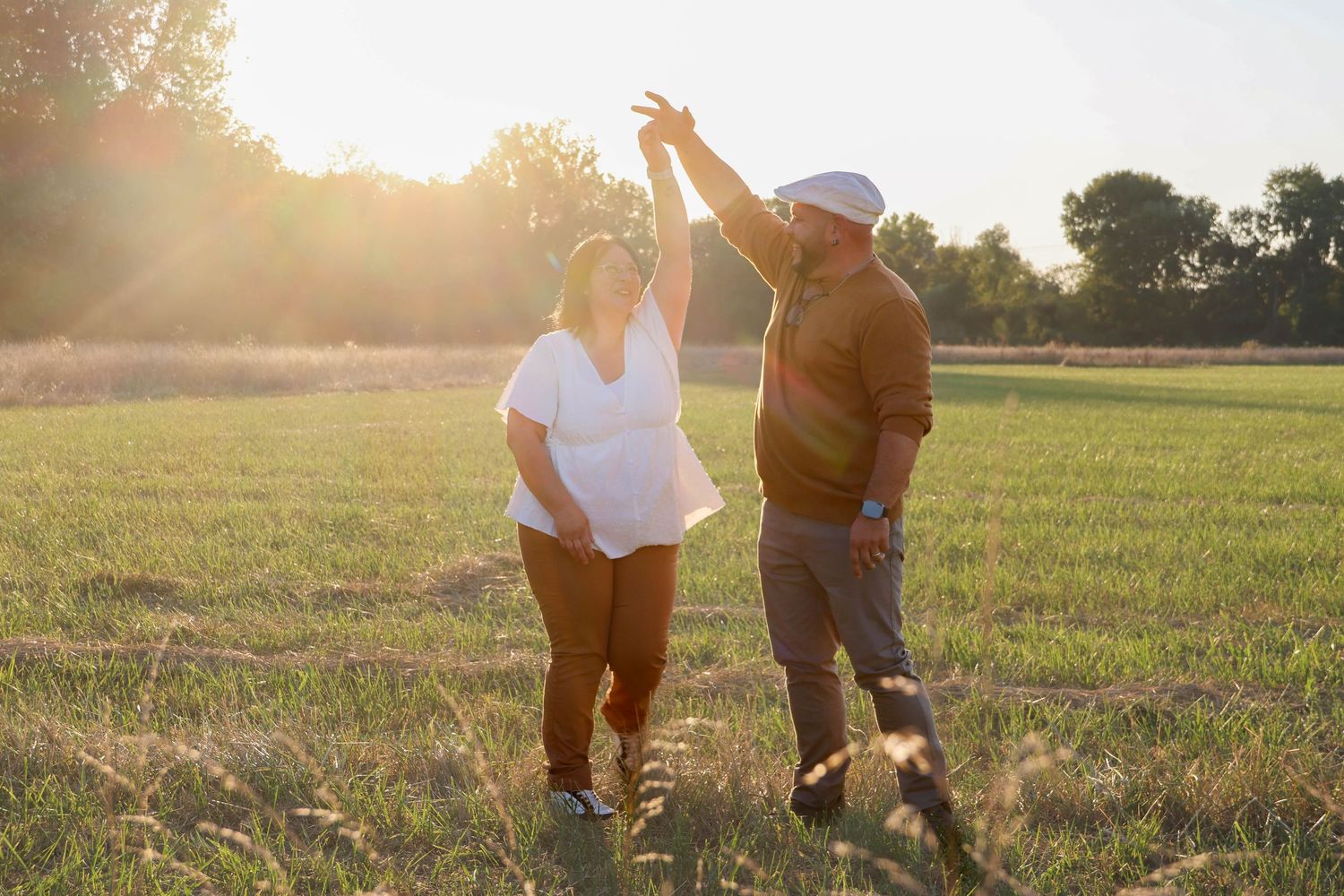Séance couple lifestyle — couple dansant joyeusement dans un champ verdoyant à l'heure dorée, photographe Châlons-en-Champagne Marne.
