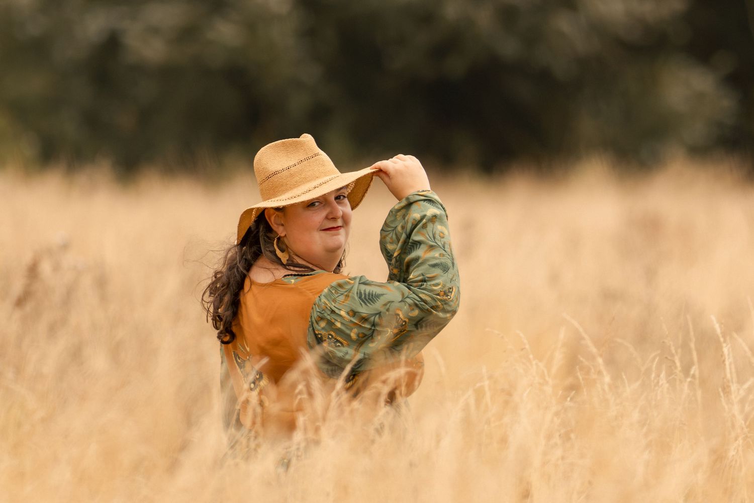 Woman in cowboy hat and camo shirt standing in golden field of tall grass.