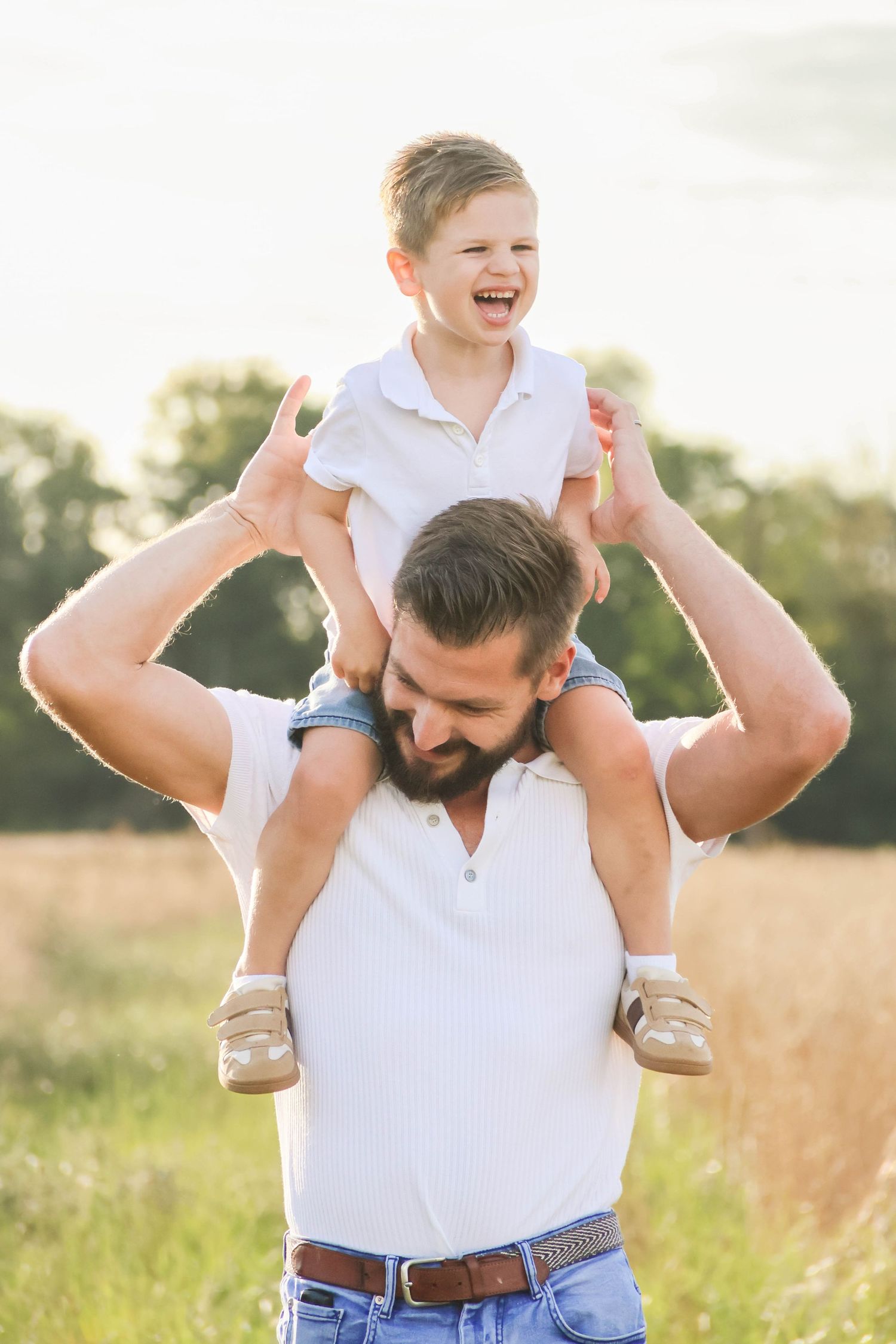 Séance famille — enfant riant sur les épaules de son papa barbu dans un champ ensoleillé, photographe famille Aisne Guignicourt.
