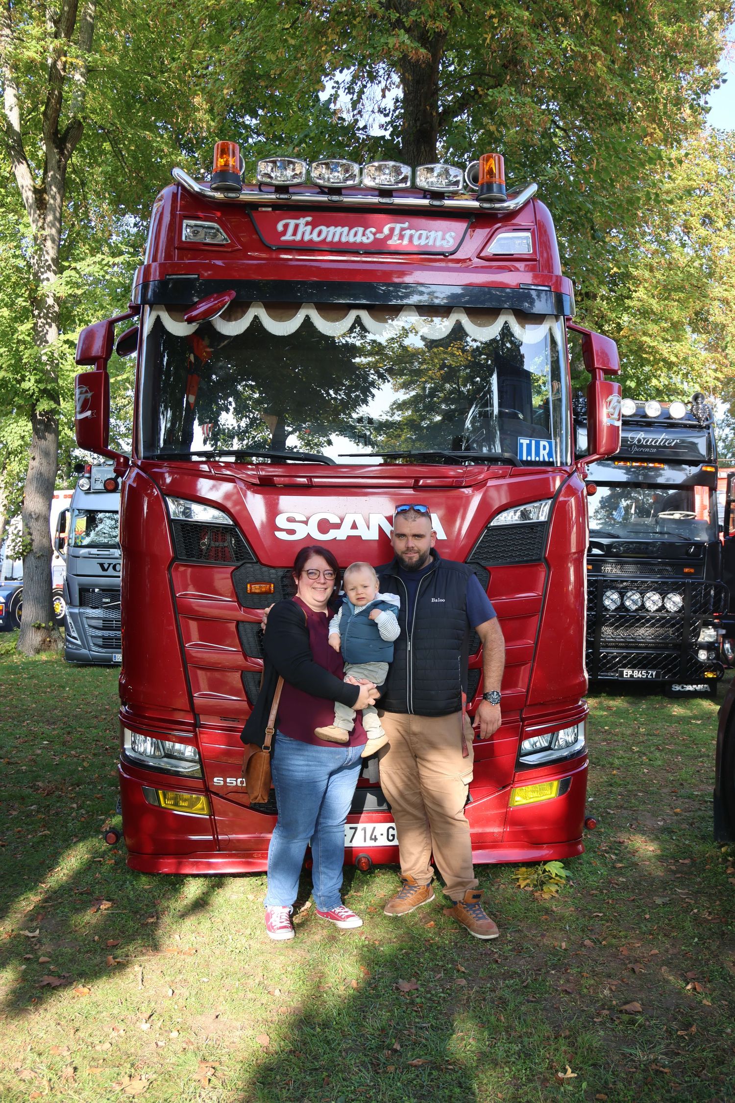 Family of three posing in front of a red Scania truck named Thomas Trons.