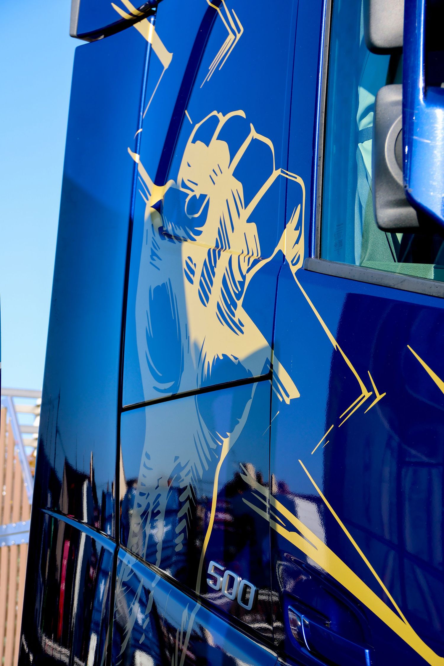 Close-up of a glossy blue truck cab door featuring a gold lion artwork design with 500 badge detail.