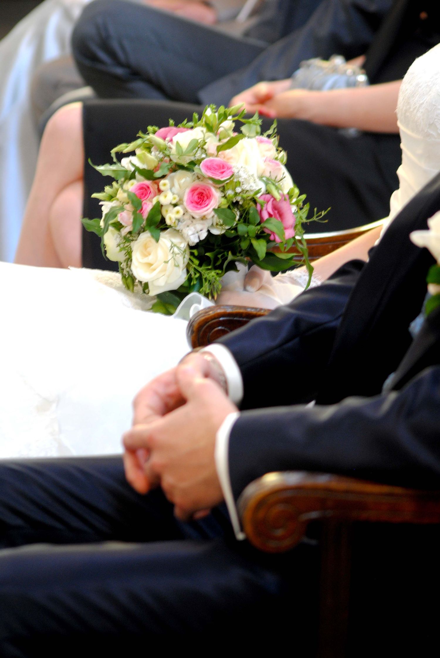 A bride holding a pink and white rose bouquet beside a groom in a navy suit during a ceremony.