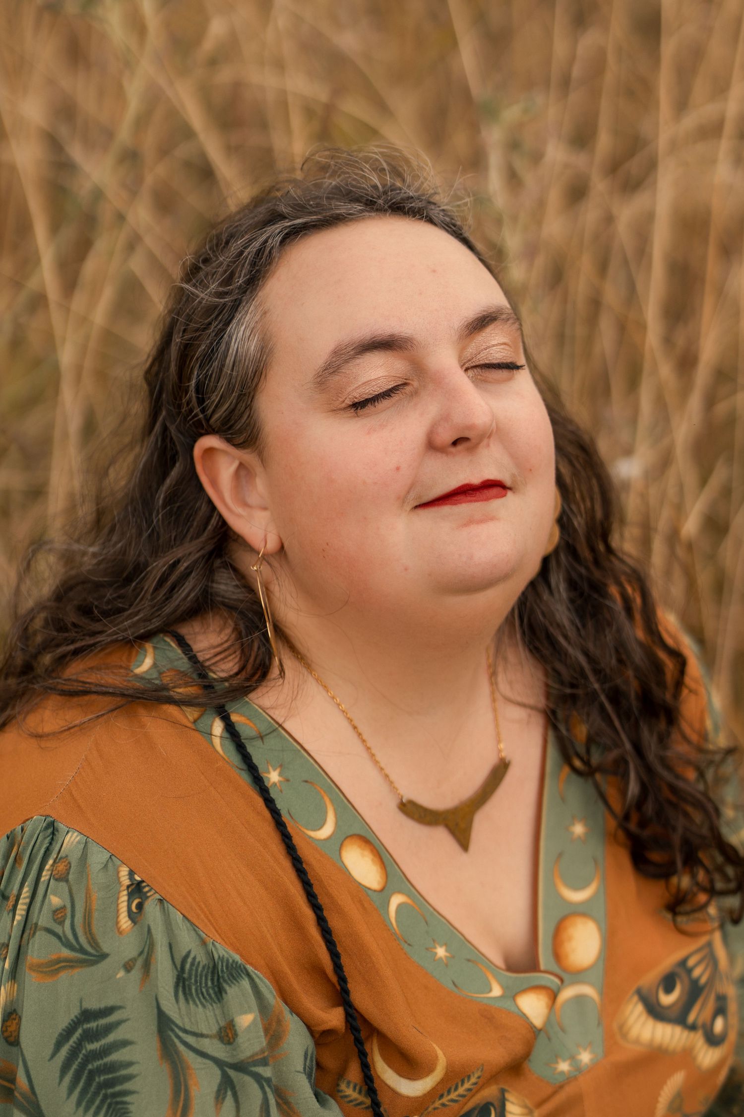 Woman with eyes closed wearing moon necklace and mustard dress in golden field.