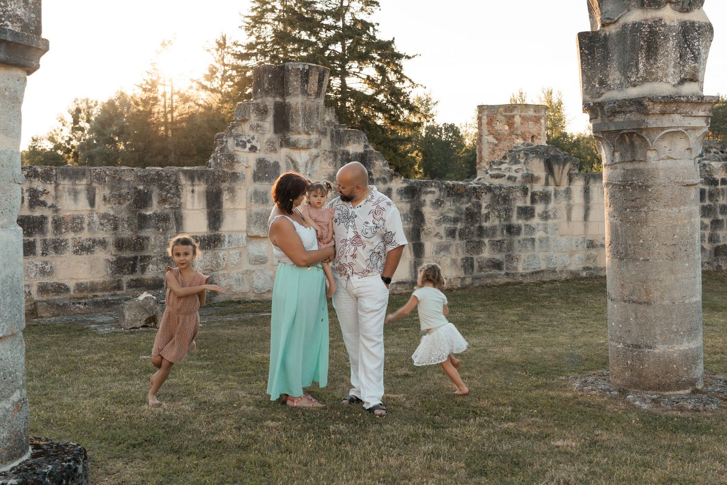 Family of five enjoys golden hour among ancient stone ruins and columns in grassy field.