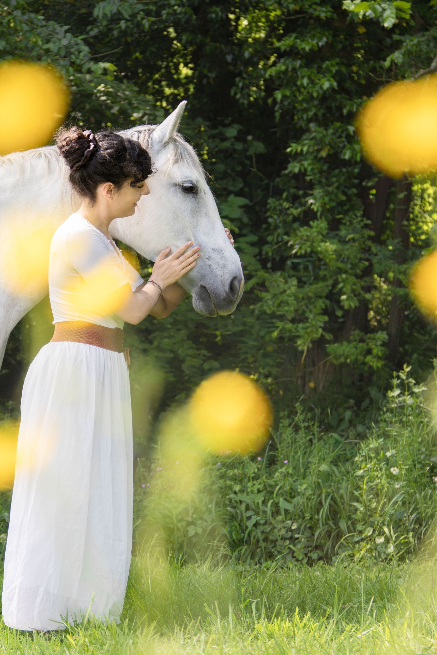 Séance cheval lifestyle — jeune femme en tenue blanche caressant doucement le museau d'un cheval blanc dans une prairie ensoleillée