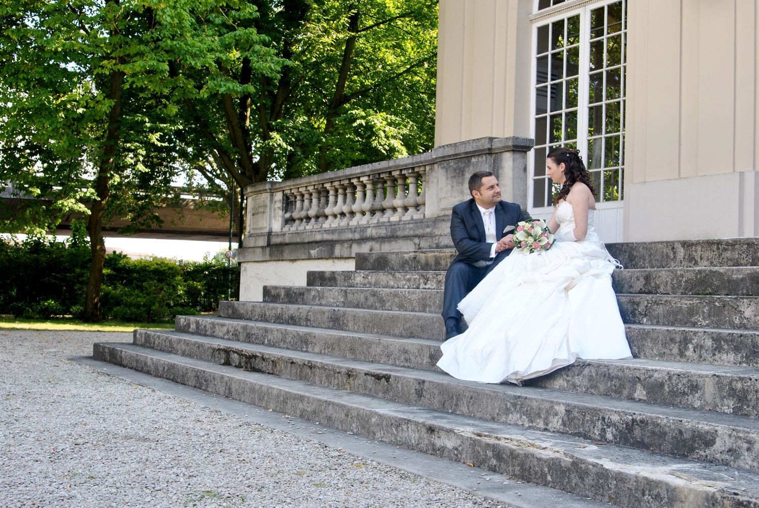 Bride and groom sit together on stone steps of an elegant building.