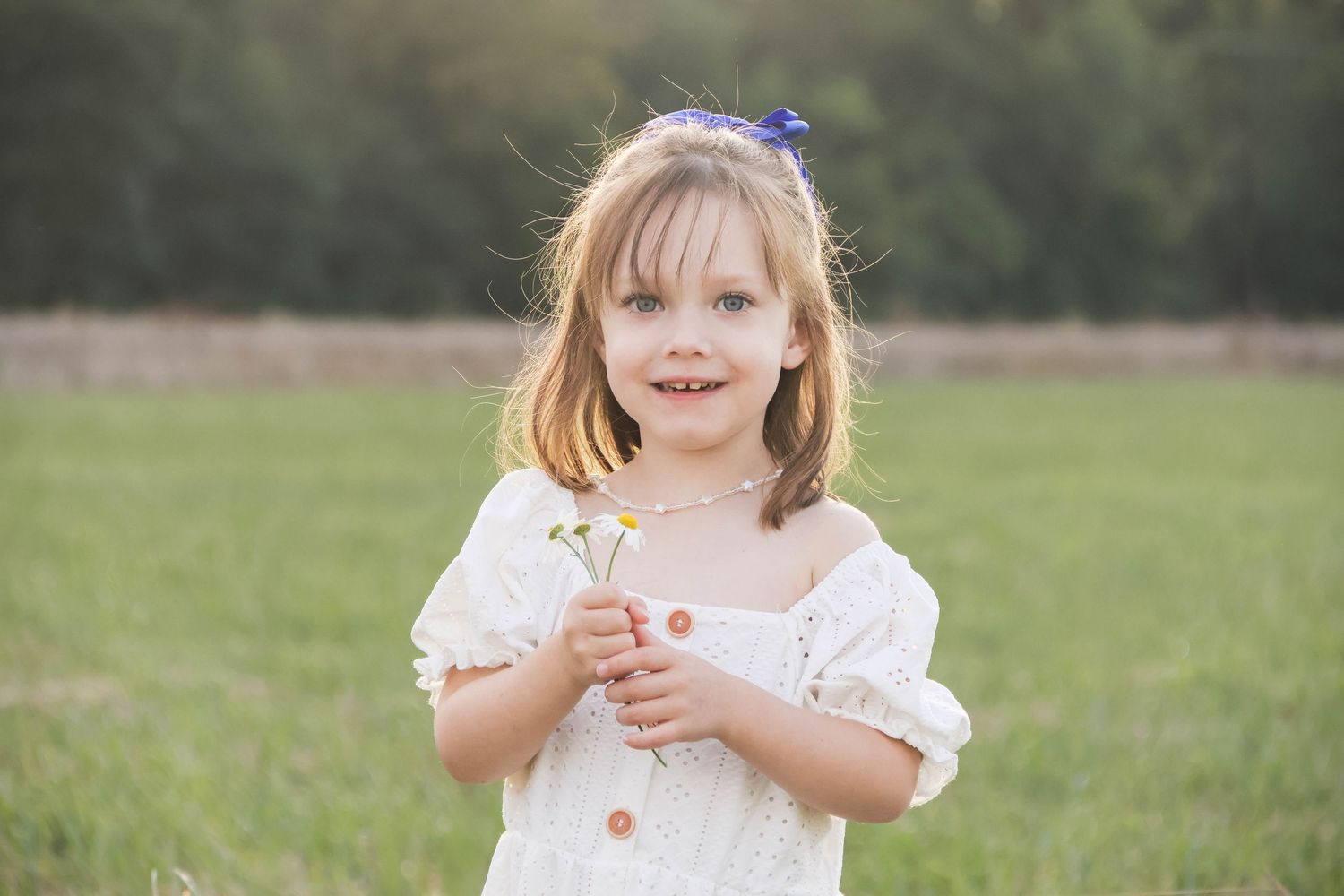 Séance famille lifestyle — fillette souriante en robe tenant des fleurs sauvages dans une prairie ensoleillée, photographe Guignicourt