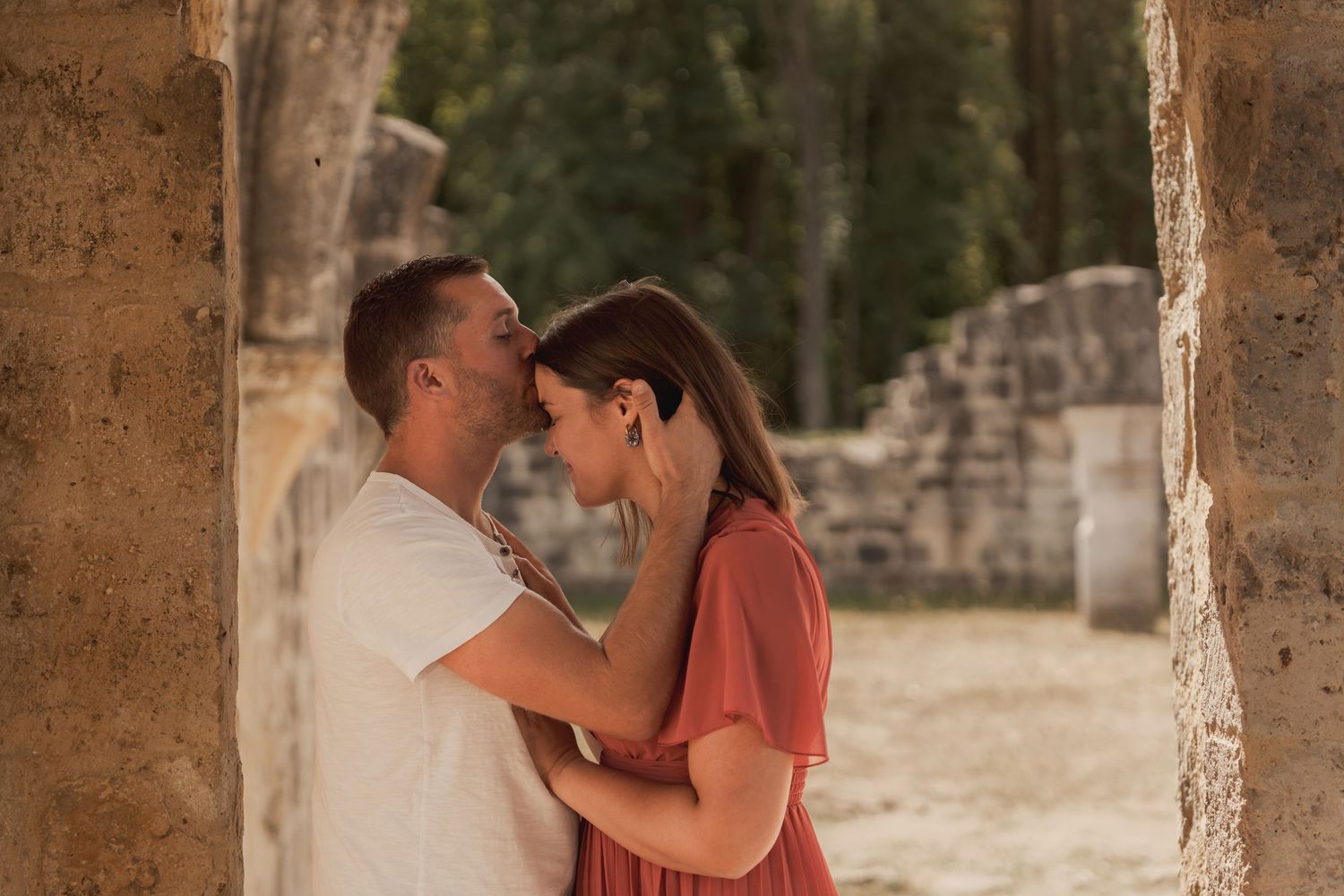 Romantic couple sharing an intimate moment among ancient stone ruins, the woman in a red dress embracing her partner.