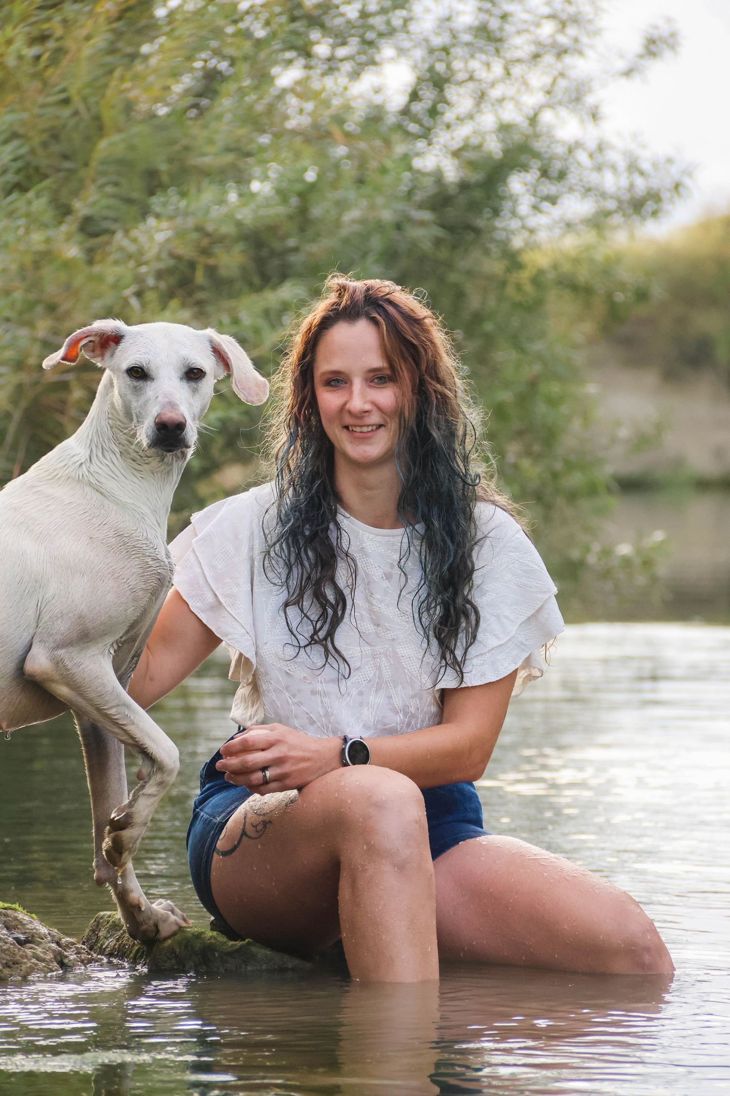 Séance animaux lifestyle — femme souriante aux cheveux longs dans une rivière avec son chien blanc, photographe Châlons-en-Champagne Marne