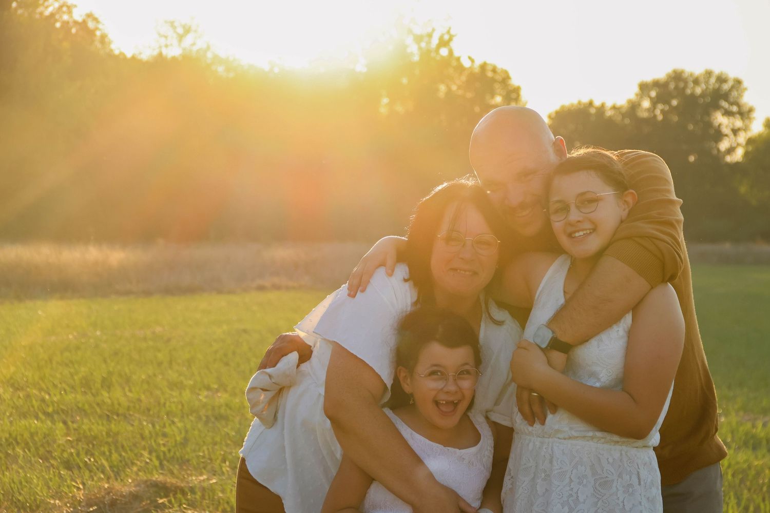 Séance famille lifestyle — famille de quatre souriante enlacée dans une prairie dorée au coucher du soleil, photographe Laon Aisne.