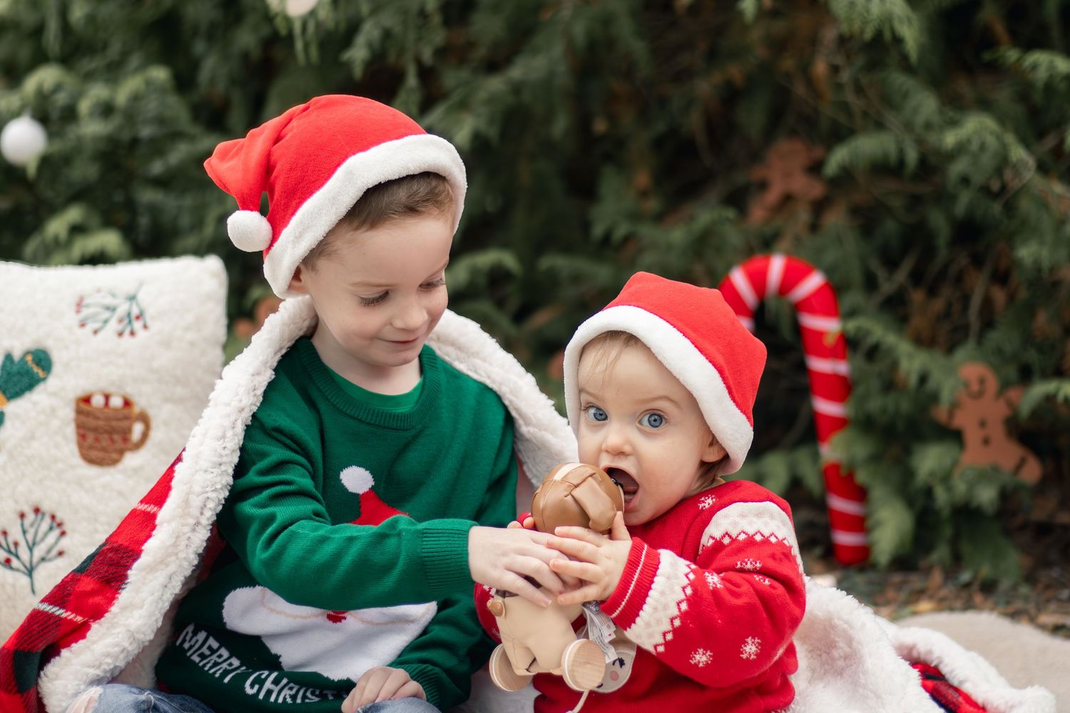 Two young siblings in Santa hats sharing a gingerbread cookie during a Christmas photo session outdoors.