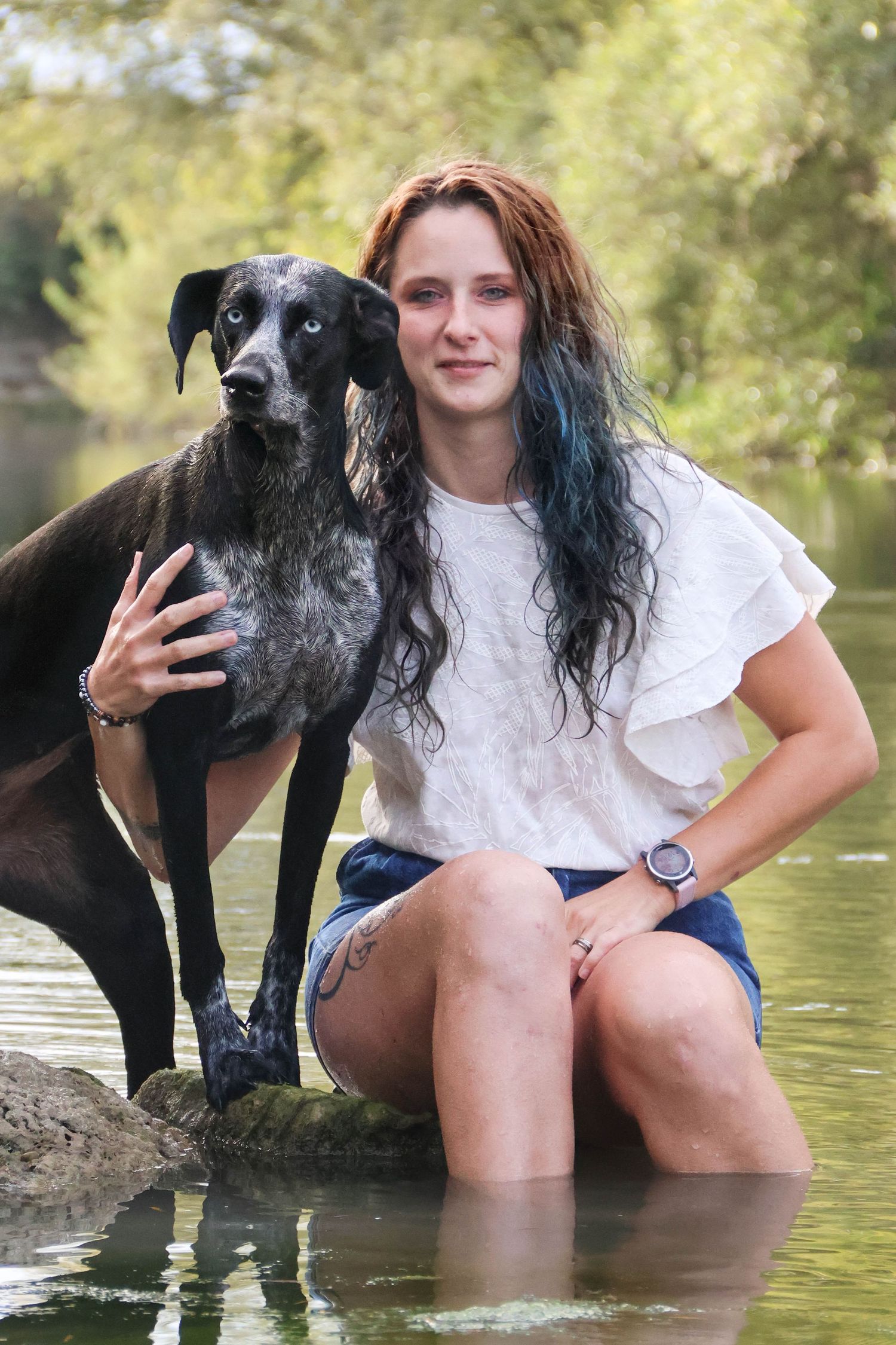 Séance animaux lifestyle — jeune femme agenouillée dans l'eau serrant son chien noir dans les bras, photographe Reims Marne.