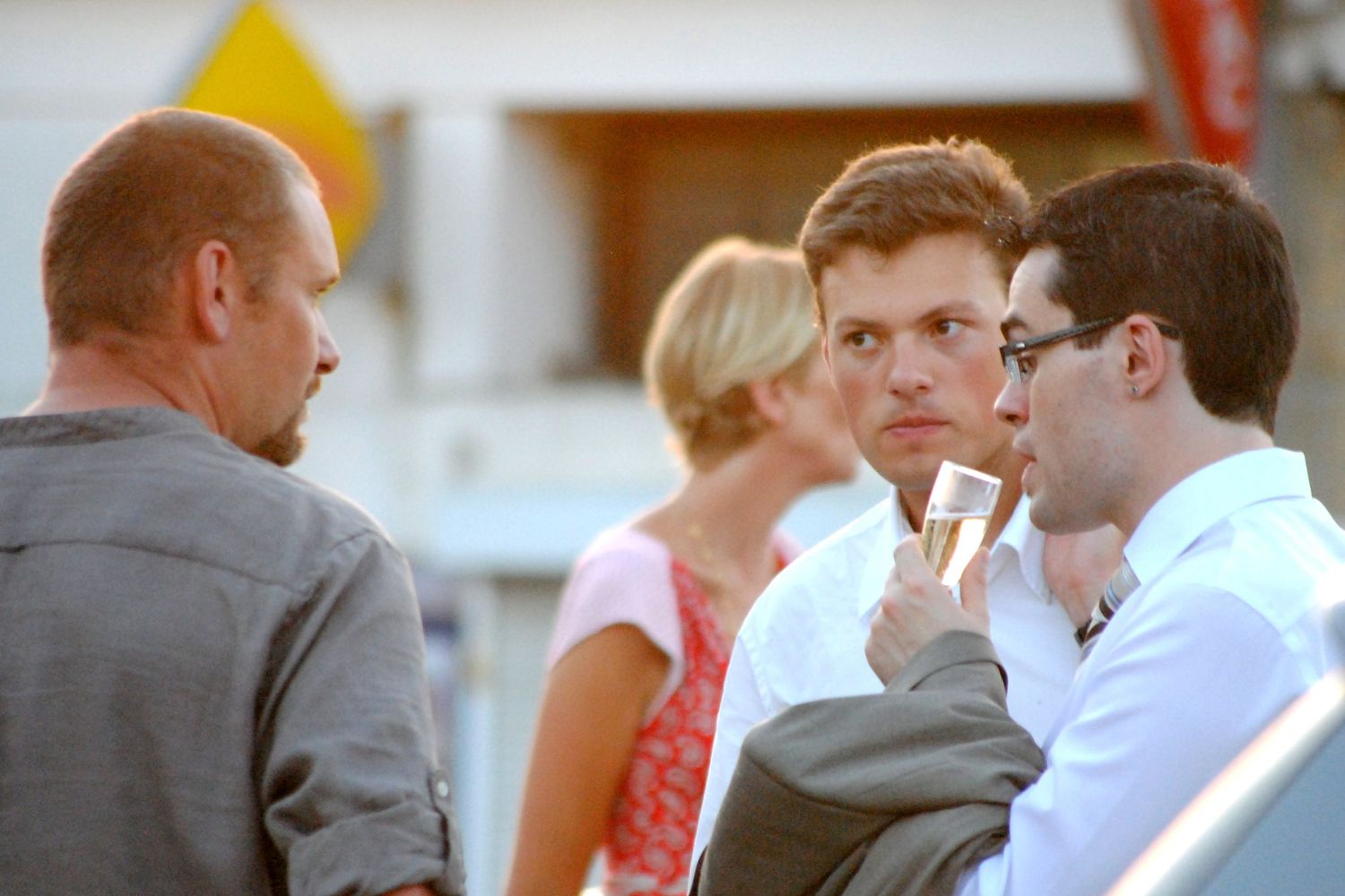 Three men in formal attire conversing at an outdoor wedding cocktail hour.