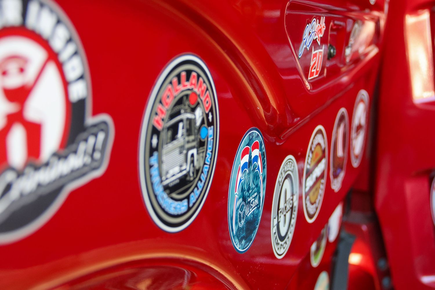 Close-up of colorful travel stickers and badges displayed on a shiny red truck exterior.