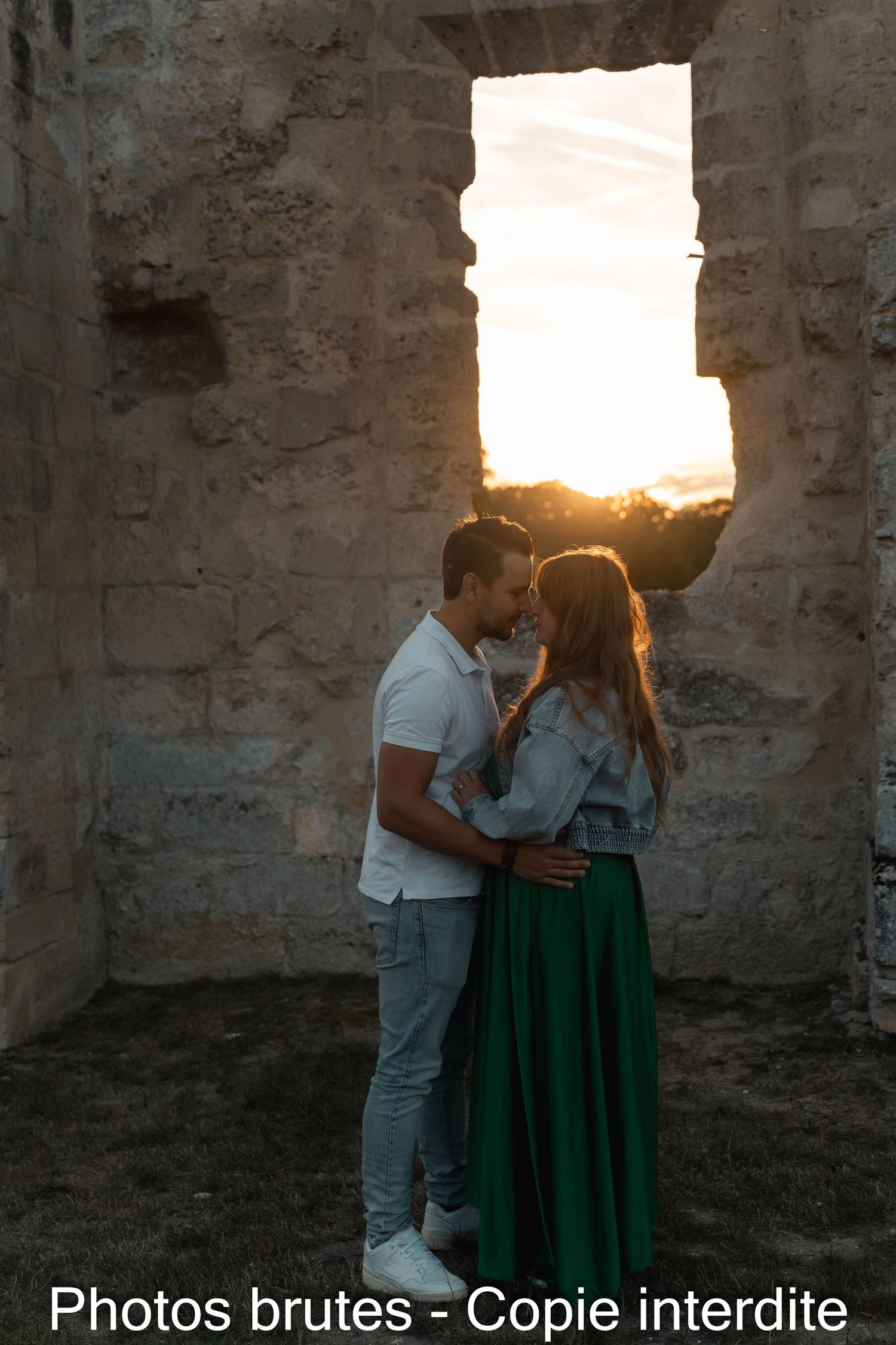 Romantic couple sharing an intimate moment in ancient stone ruins with golden sunset light glowing through a large window opening.
