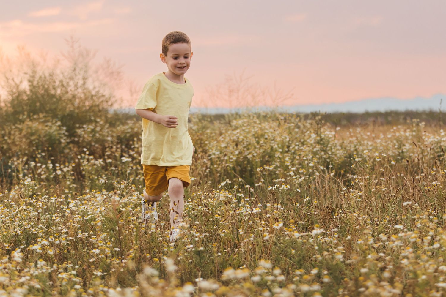 Young boy running through a wildflower meadow at sunset wearing yellow shirt and shorts.