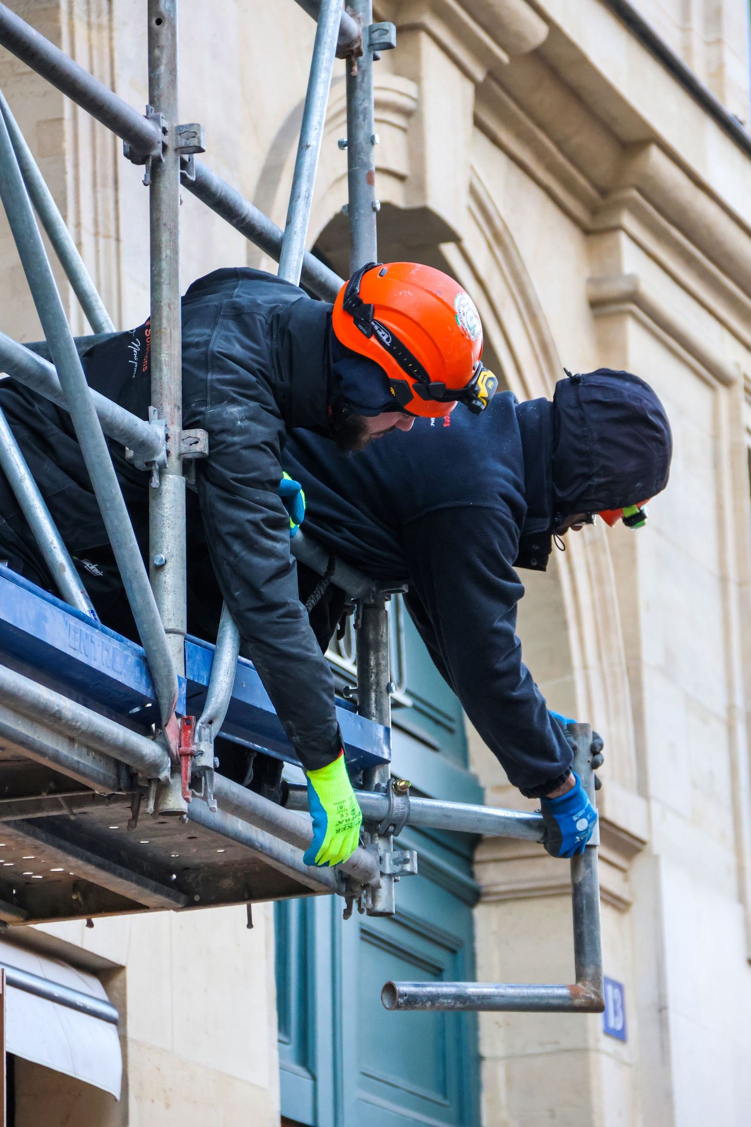 Construction worker in orange helmet on scaffolding performing maintenance on a historic building facade.