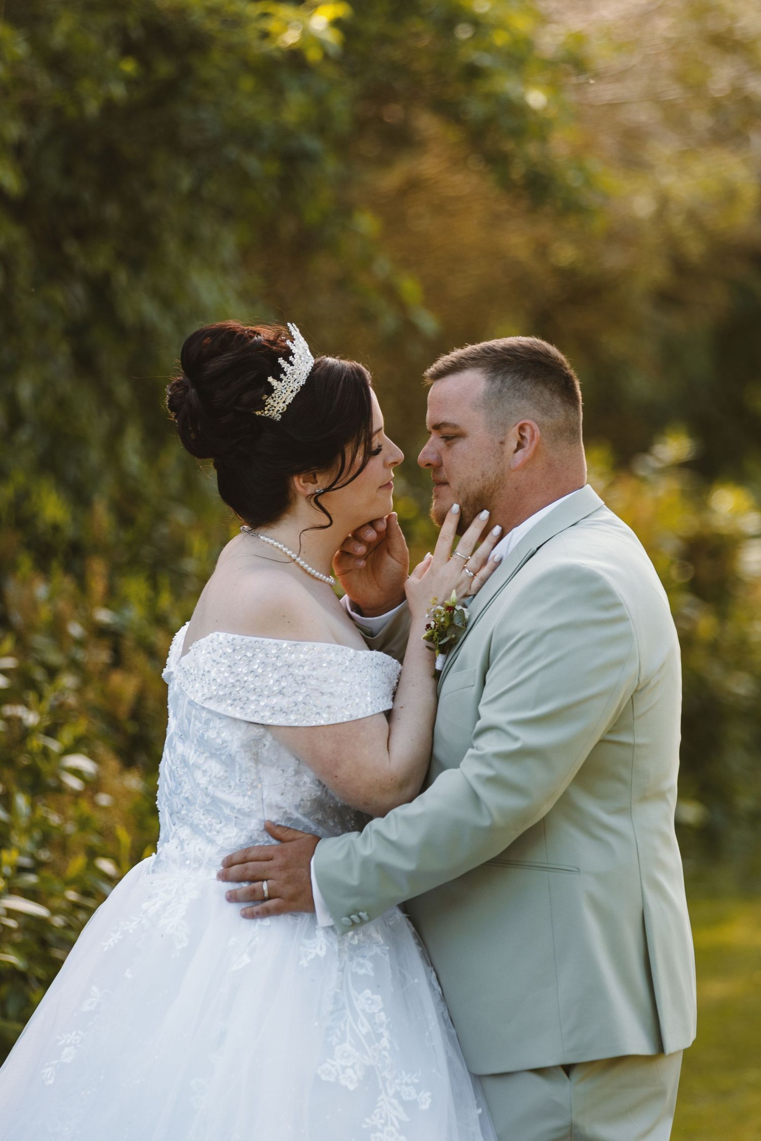 Bride and groom share a romantic moment outdoors, with the bride in a white off-shoulder gown and groom in a tan suit.