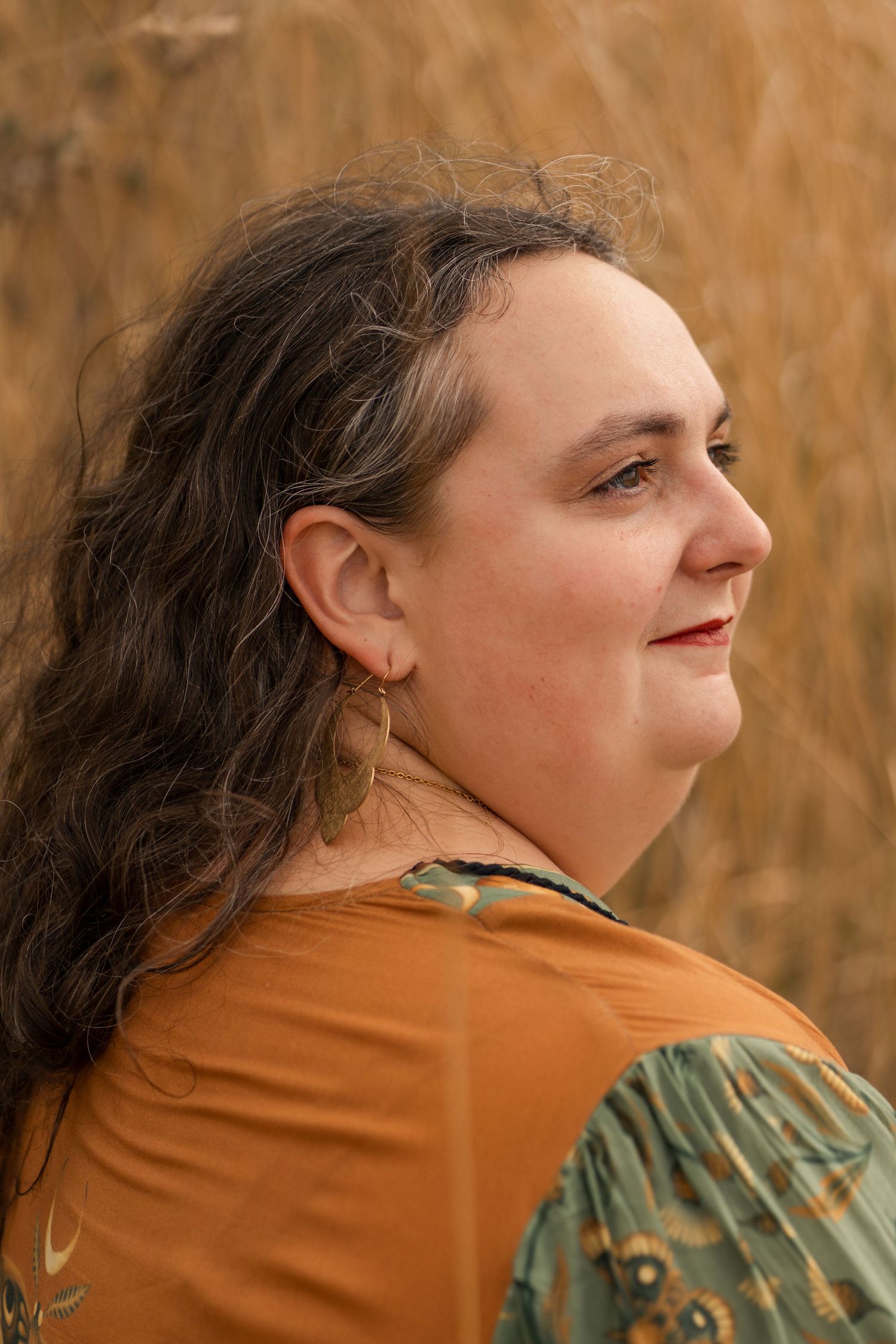Side profile of woman with curly hair in mustard top against golden grass.