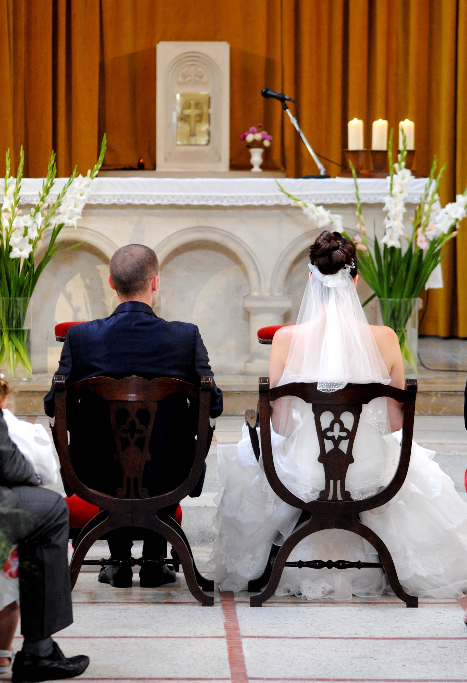 A bride and groom seated at the altar during a church wedding ceremony from behind.