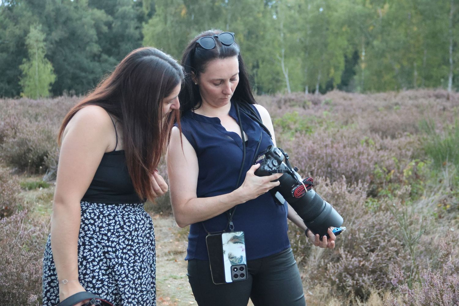 Two women reviewing photos on a camera with telephoto lens outdoors in nature.