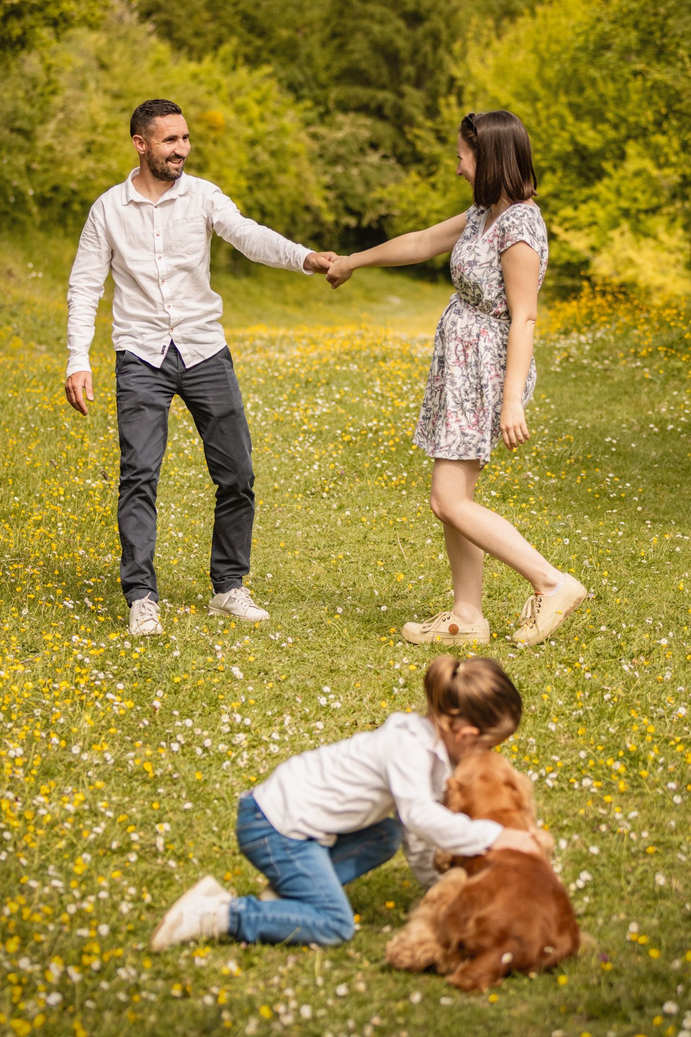 Happy family with a dog playing in a sunny meadow with yellow wildflowers on a beautiful summer day.