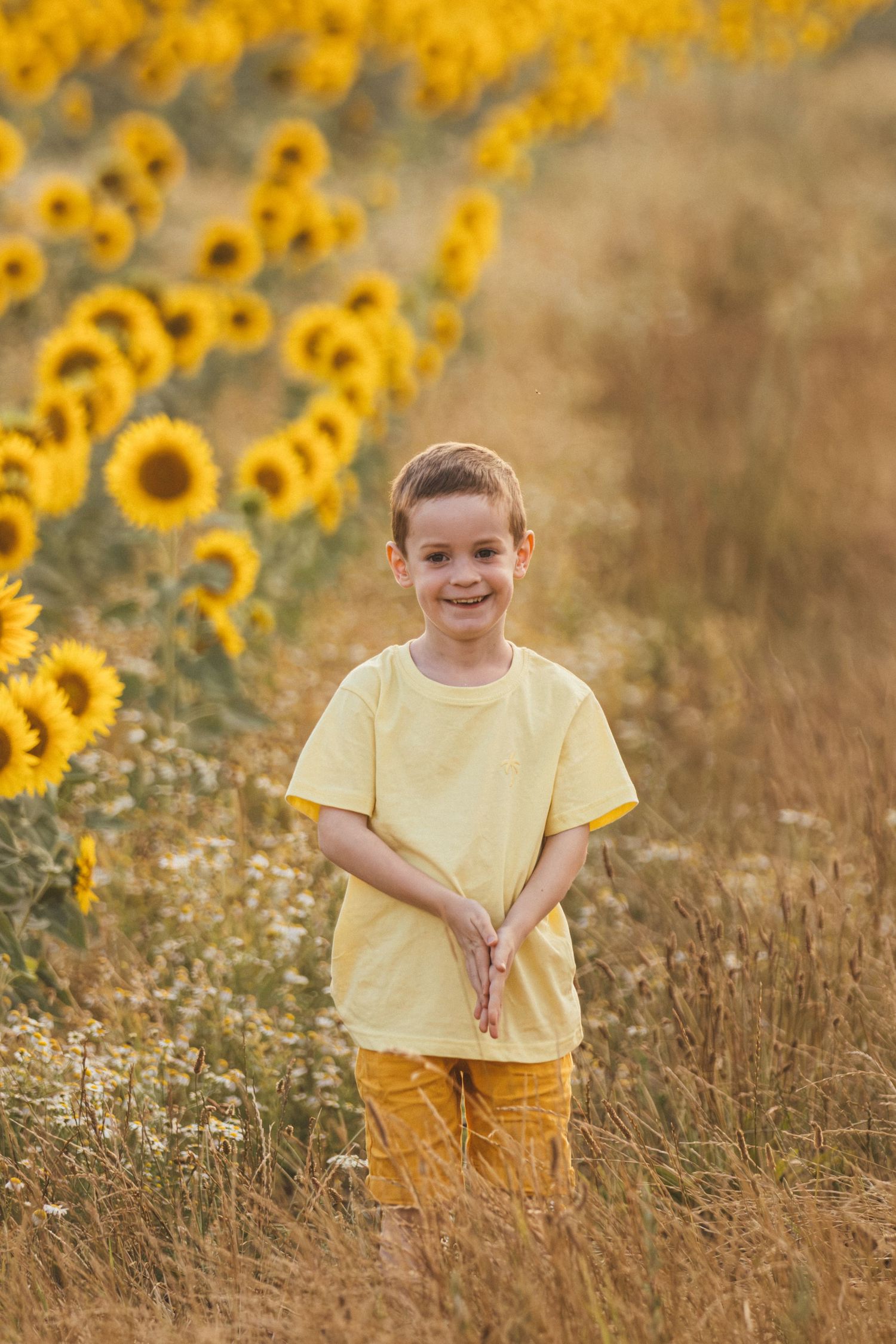 Smiling boy in yellow shirt standing in a sunflower field on a sunny day.
