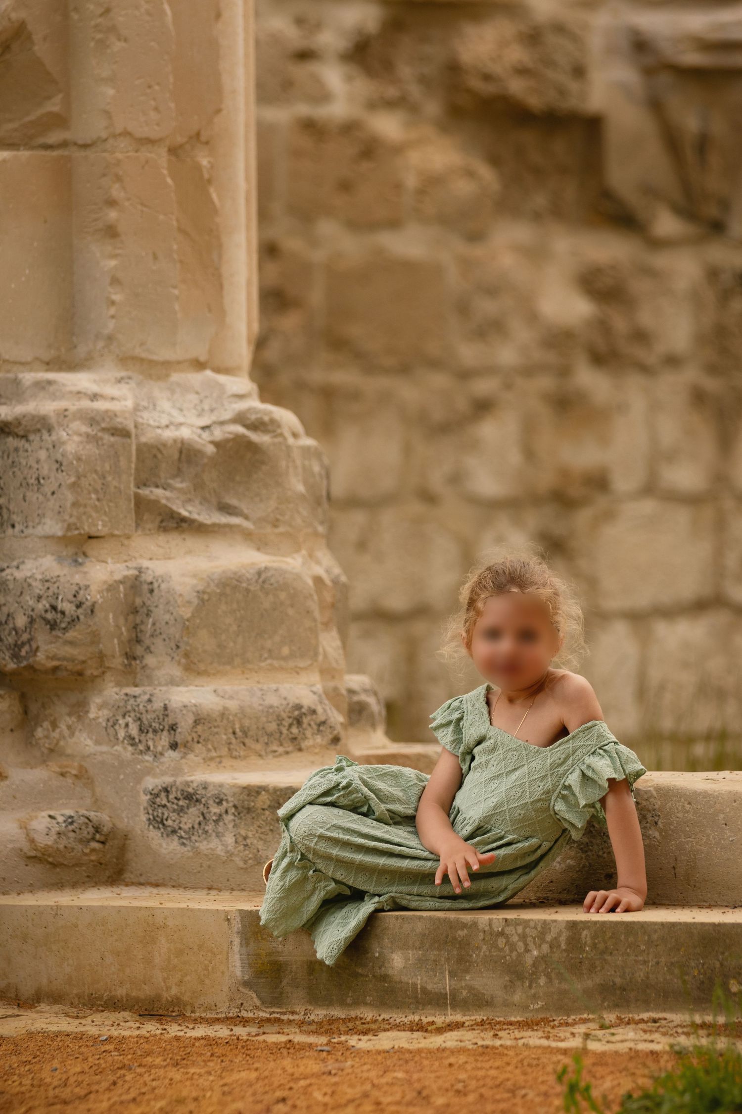 Young child in green romper sitting on ancient stone steps beside a weathered column.