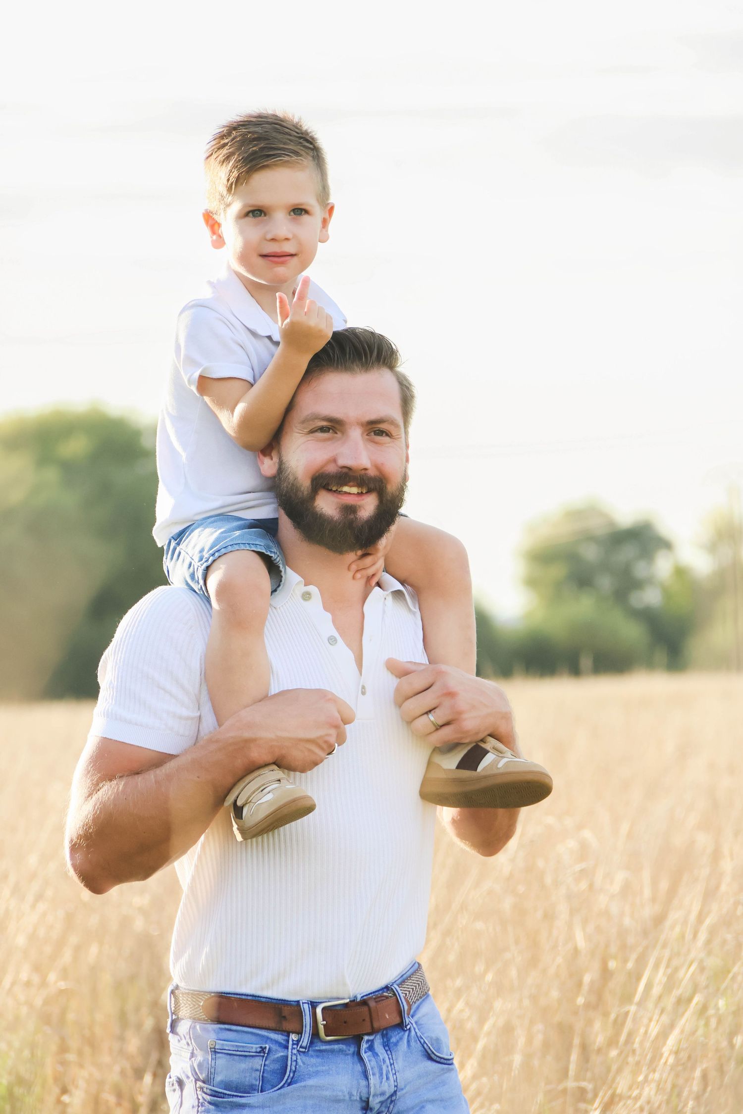 Séance famille — papa barbu souriant avec son fils assis sur ses épaules dans un champ, photographe famille Aisne Guignicourt.