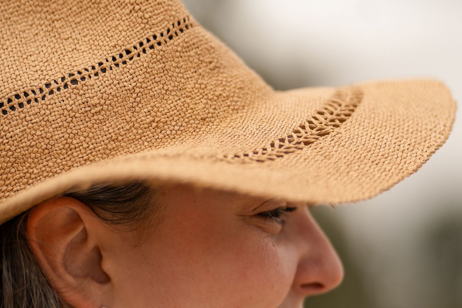 Close-up profile of a woman wearing a woven straw sun hat with decorative perforated band detail.