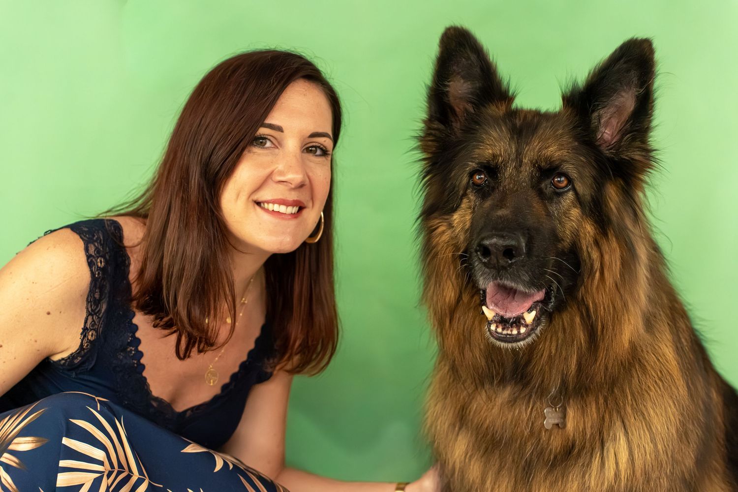 Woman with brown hair poses beside a large fluffy German Shepherd dog against a green background.