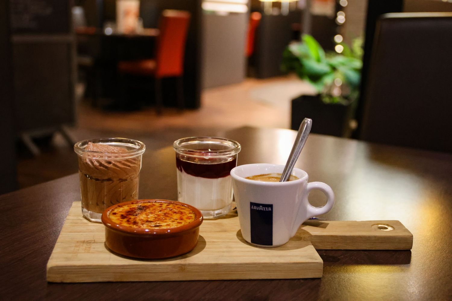 A wooden serving board with espresso, iced coffee, black coffee, and a mini tart at a cozy cafe.