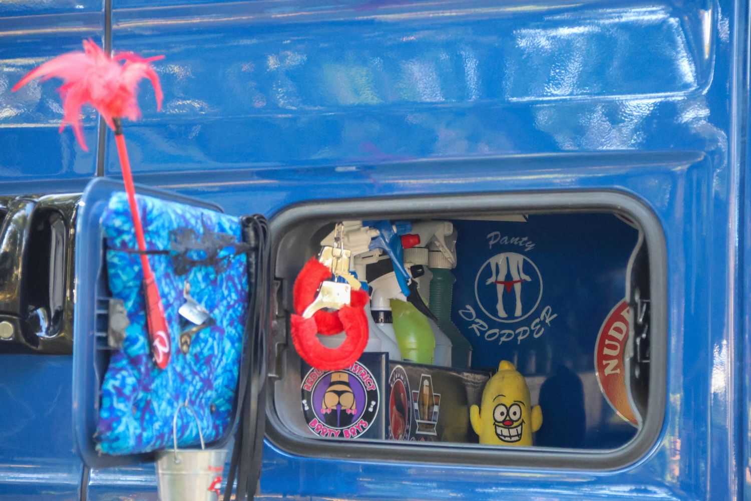 Blue truck cab window decorated with colorful stickers and hanging novelty toys.