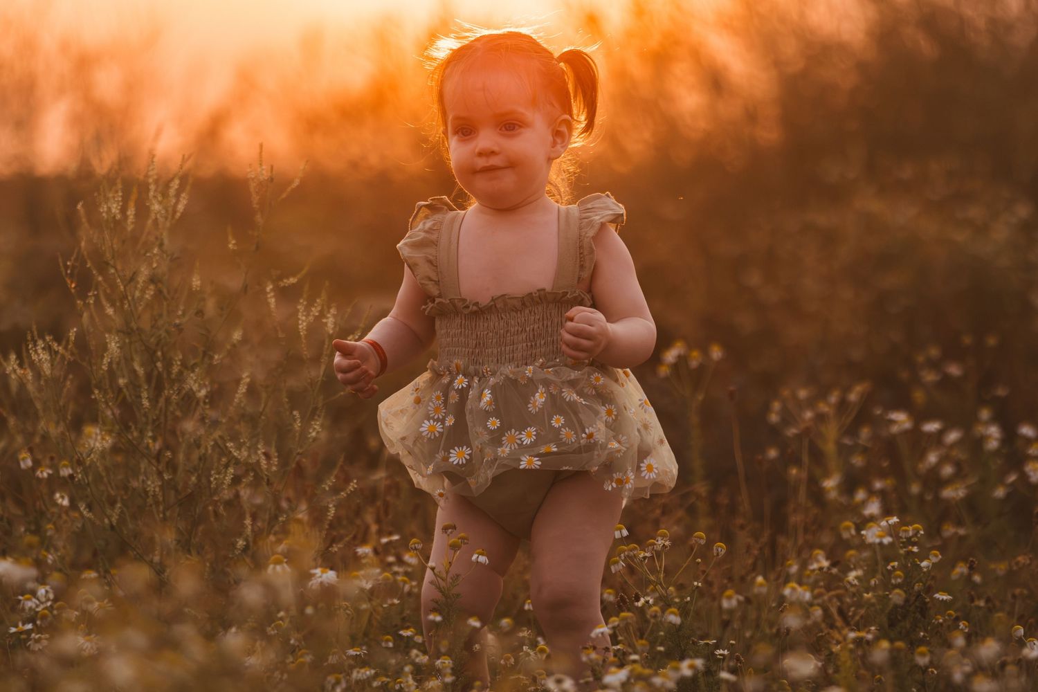 Toddler girl in floral romper running through wildflower field at golden sunset hour.